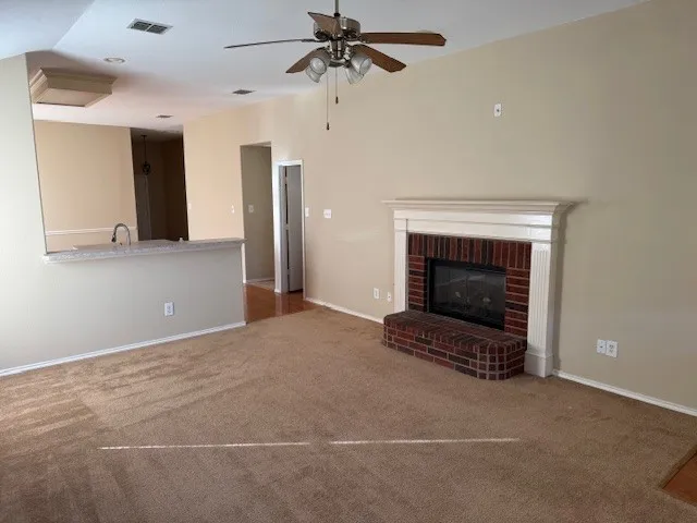 Living area featuring a brick fireplace with a white mantel, ceiling fan, and carpeted flooring