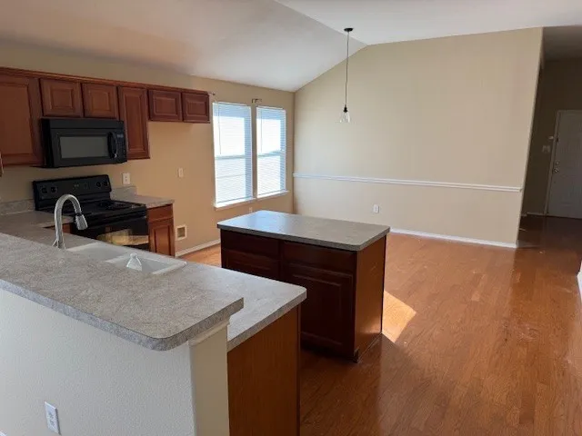 Kitchen featuring wood-finish cabinetry, light-toned countertops, a stainless steel sink with a gooseneck faucet, and black appliances including a range and microwave
