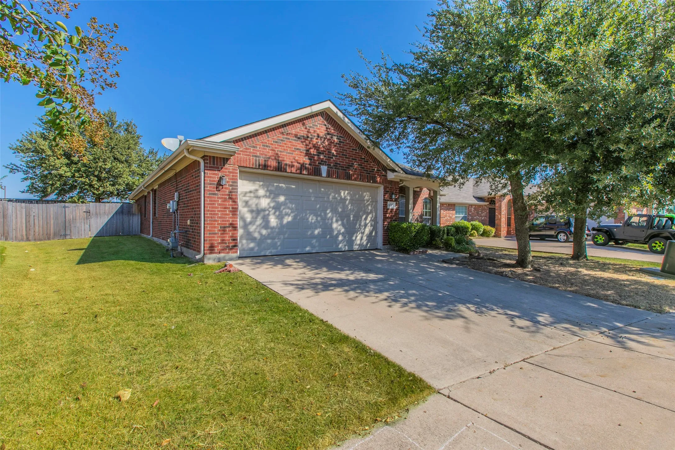 Brick exterior residence with an attached garage, concrete driveway, and established front landscaping