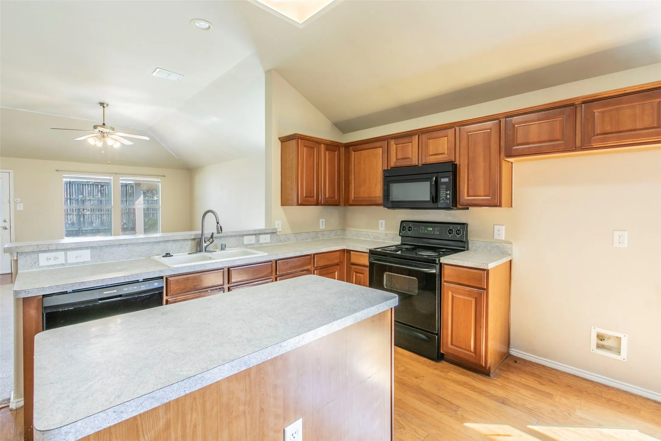 Kitchen featuring warm-toned cabinetry, light-colored countertops, and black appliances