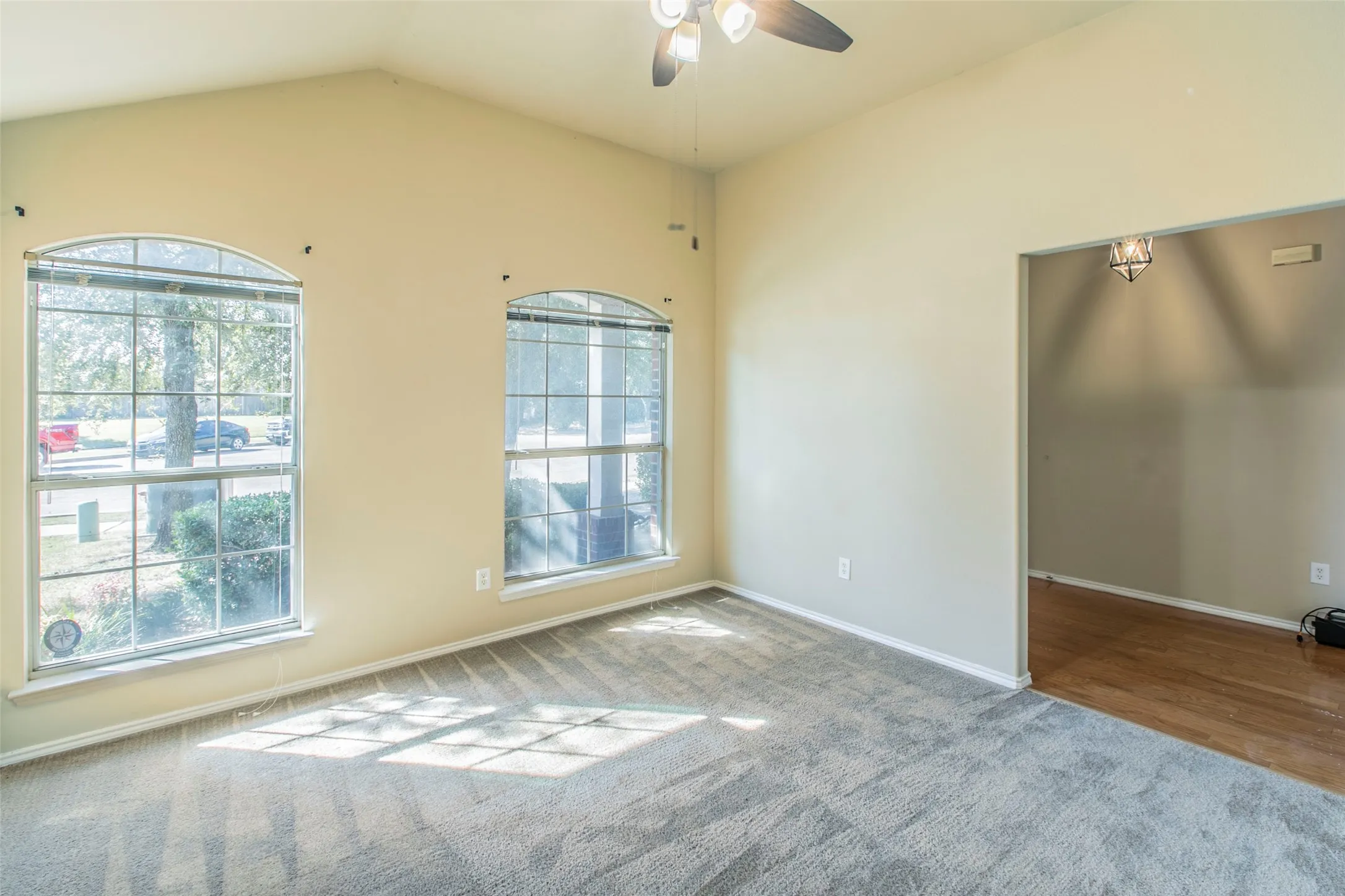 Vaulted ceilings with a ceiling fan, two arched windows, light-toned walls, and grey carpeting