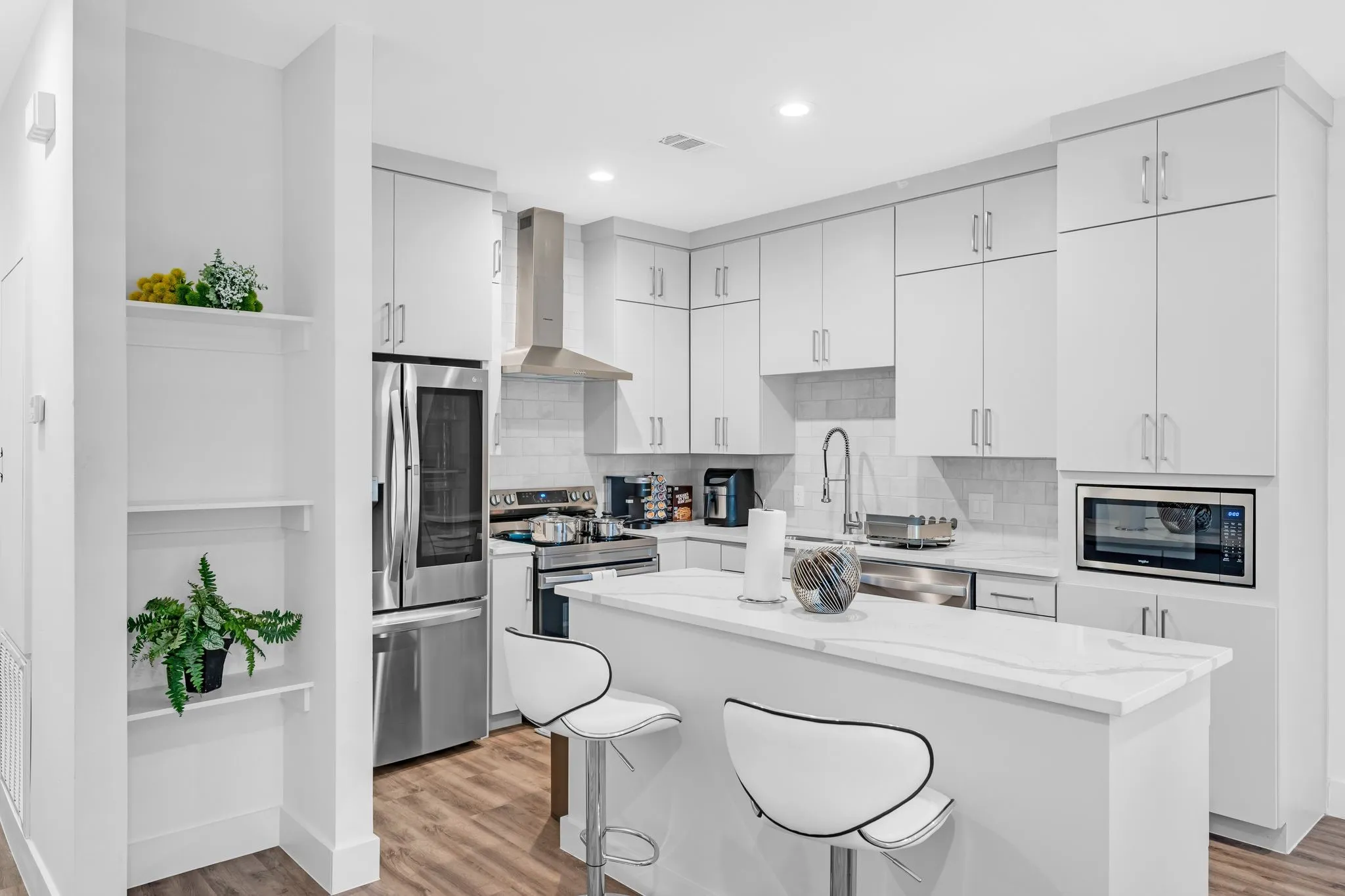 The kitchen features white cabinetry, stainless steel appliances, a white tile backsplash, and a kitchen island with a white countertop