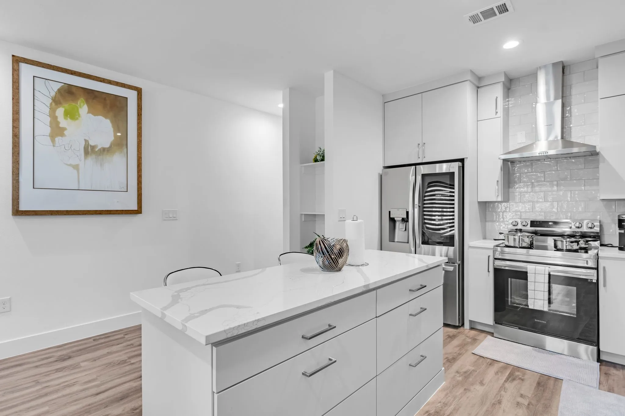 The kitchen features a center island with a stone countertop, light-colored cabinetry, stainless steel appliances, and wood-style flooring