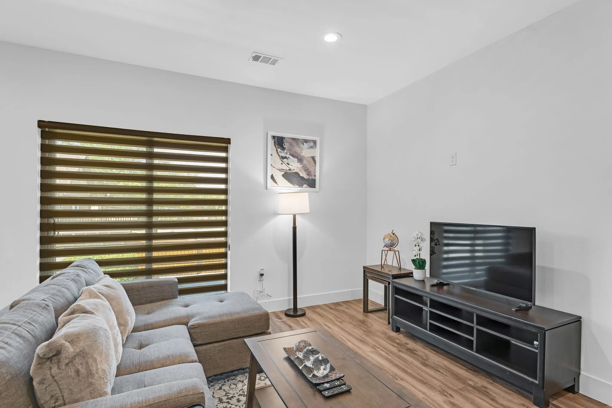 This living area features a large window with horizontal blinds, wood-look flooring, and recessed ceiling lighting