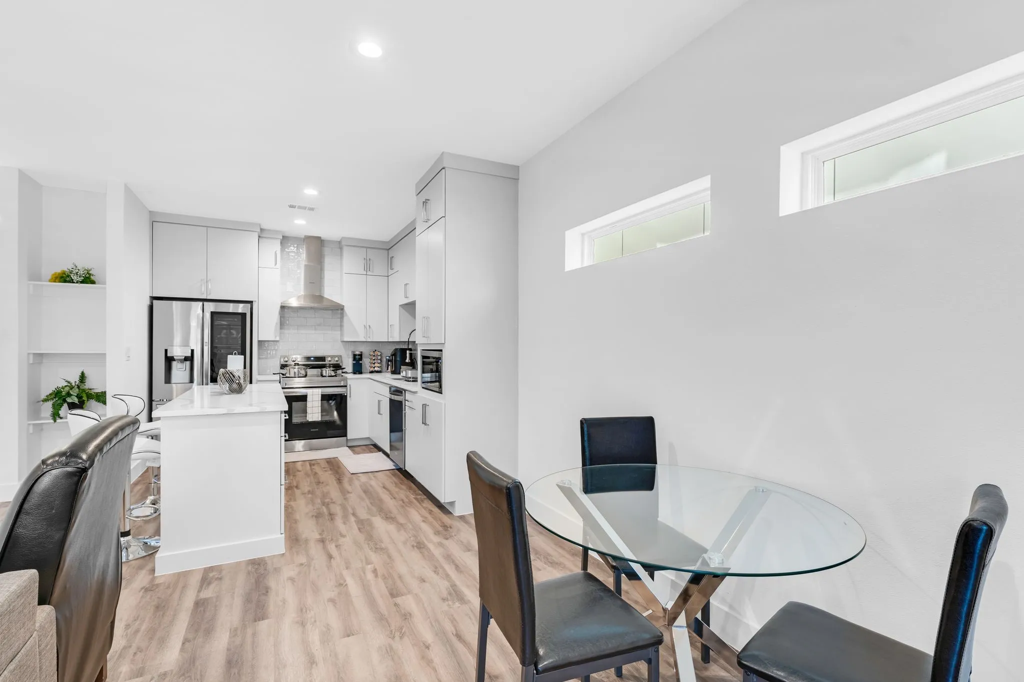 Modern kitchen with light wood-style flooring, white cabinetry, stainless steel appliances, and a central island with white countertops