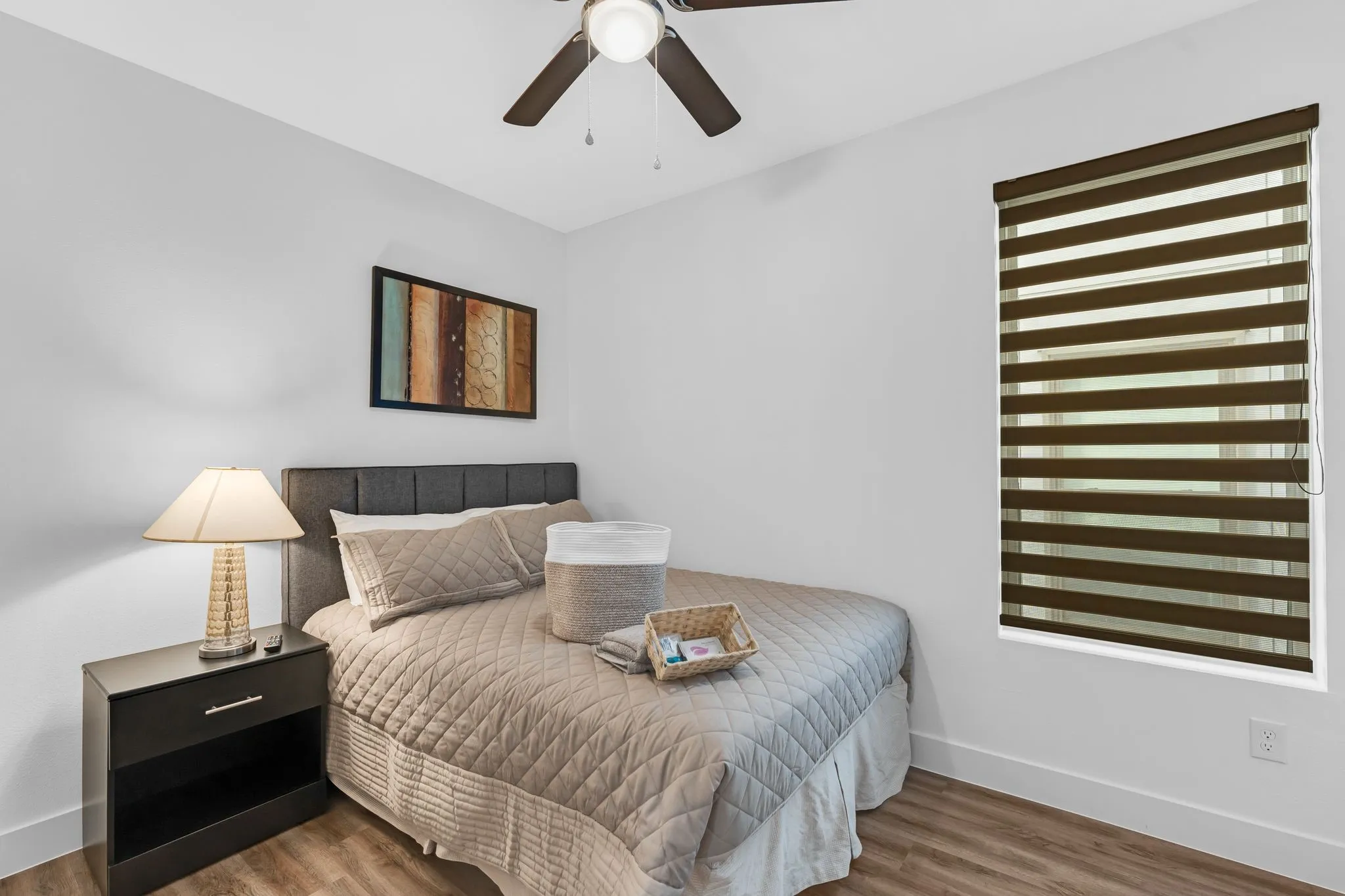 This room features light-colored walls, wood-style flooring, and a ceiling fan with a light fixture