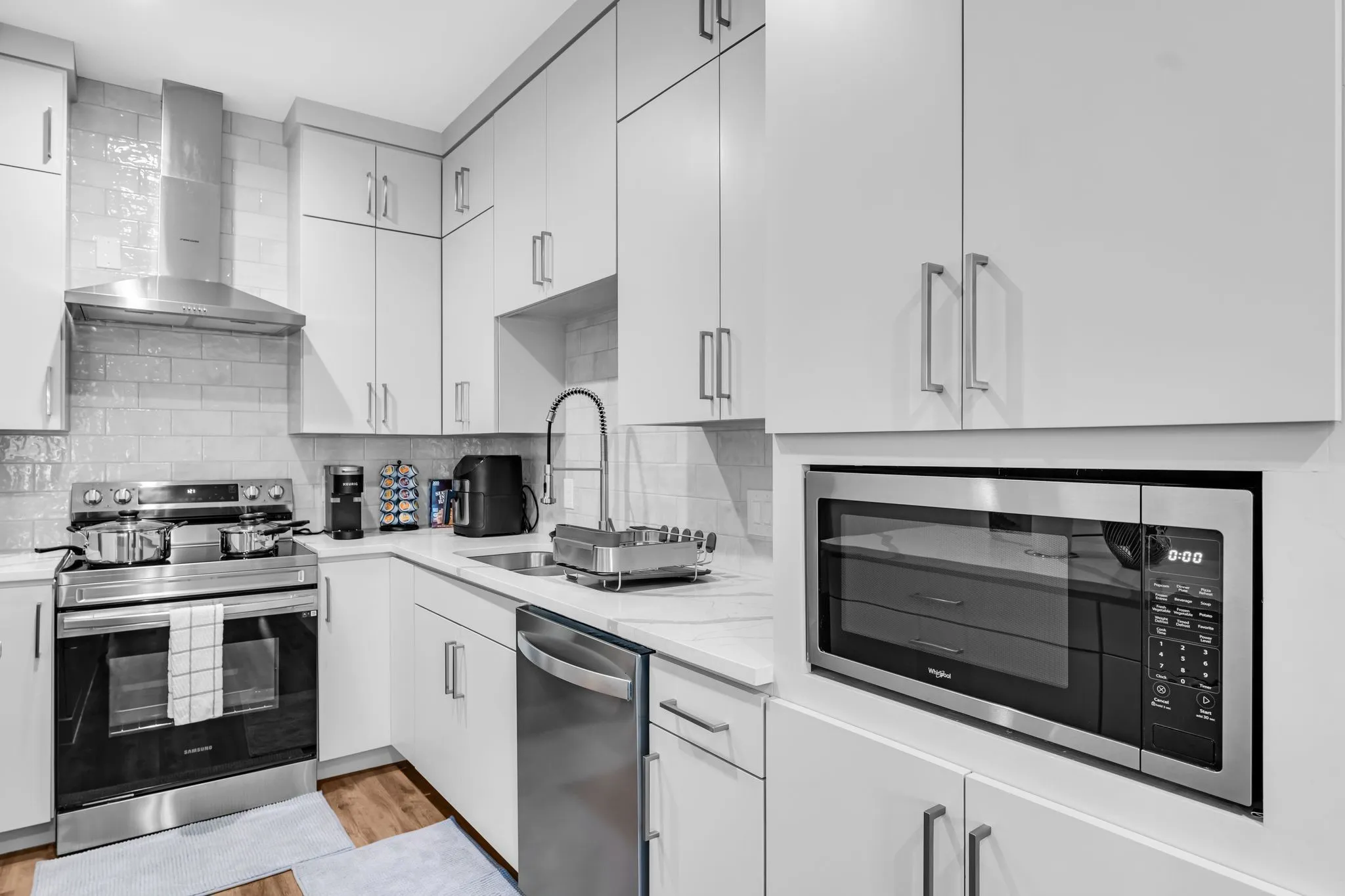 The kitchen features ample white cabinetry, a stainless steel range with an overhead hood, a stainless steel microwave, and white countertops