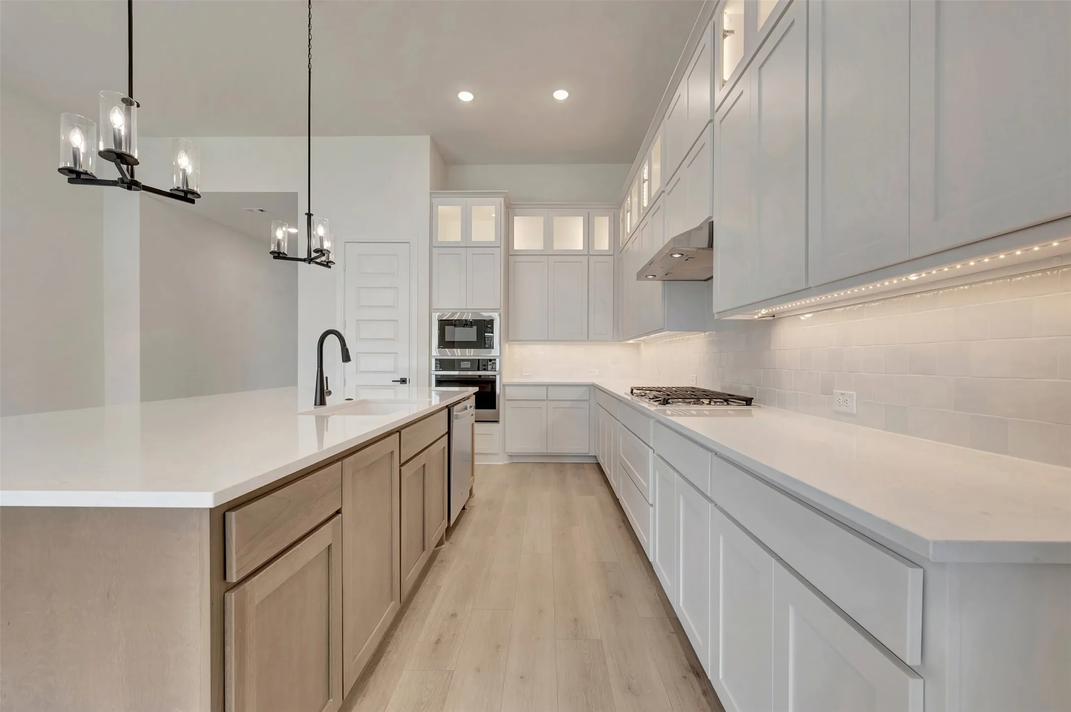 Modern kitchen featuring light wood-finish flooring and a spacious island with a built-in sink and matte black faucet