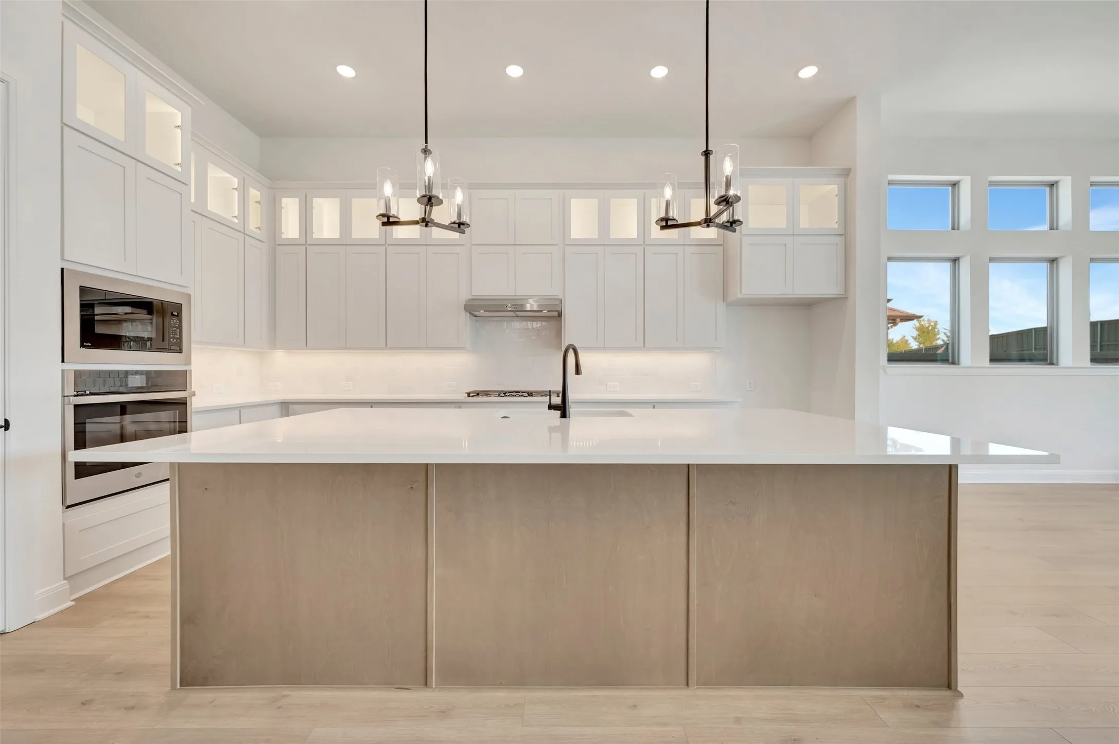 Expansive kitchen island with a light wood-finish base and light-toned countertop, complemented by white cabinetry, stainless steel appliances, and wood-finish flooring