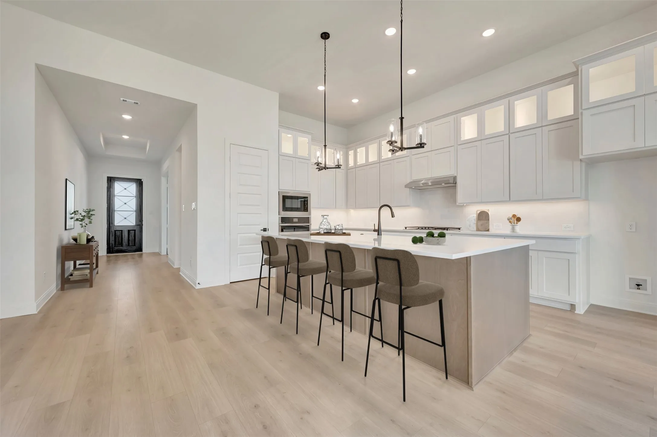 Open-concept kitchen featuring an oversized island with seating, pendant lighting, built-in stainless steel appliances, white cabinetry, and wood-finish flooring