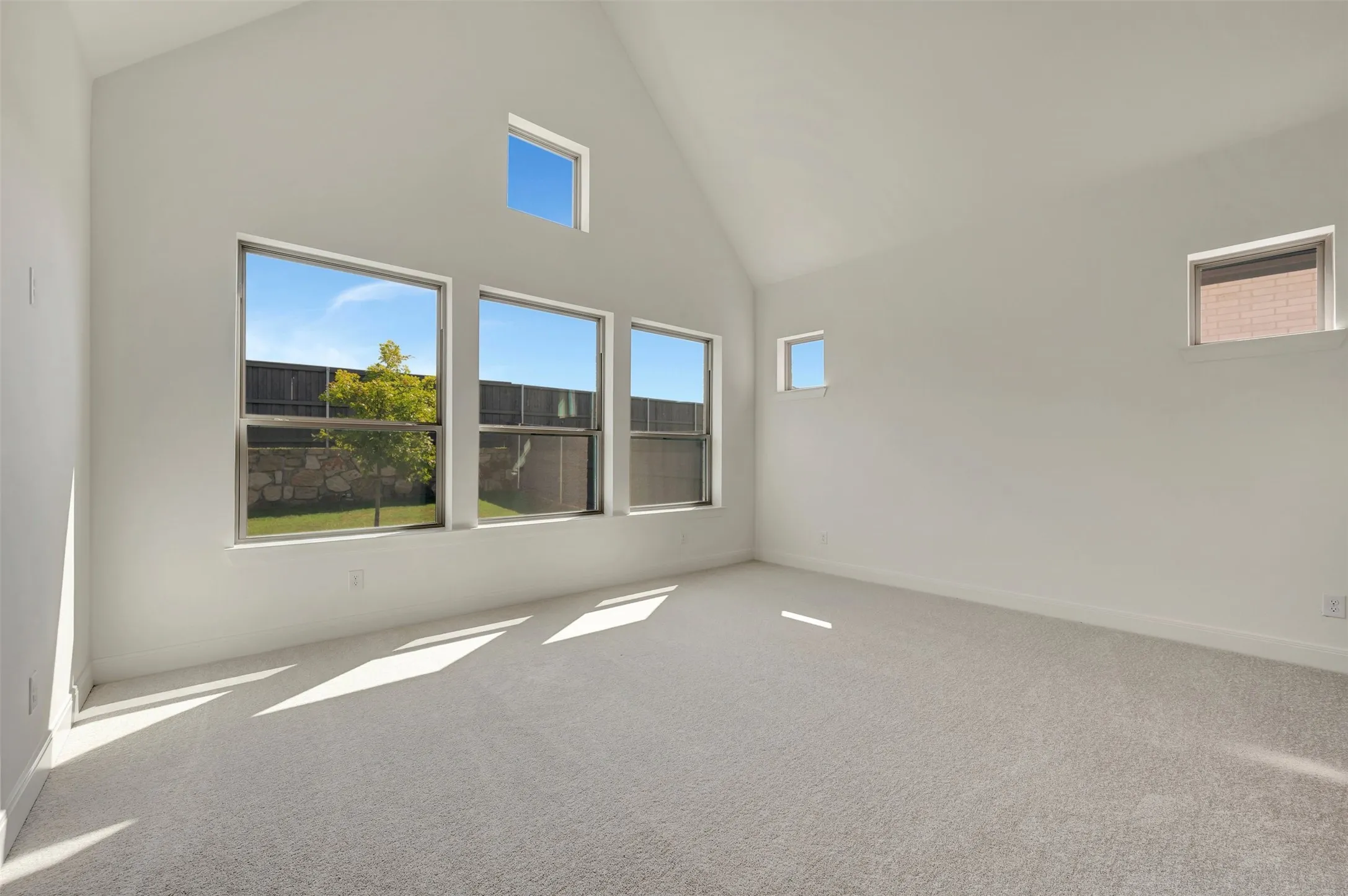 Spacious room featuring vaulted ceilings, light-colored carpeting, multiple windows, and a clear exterior view