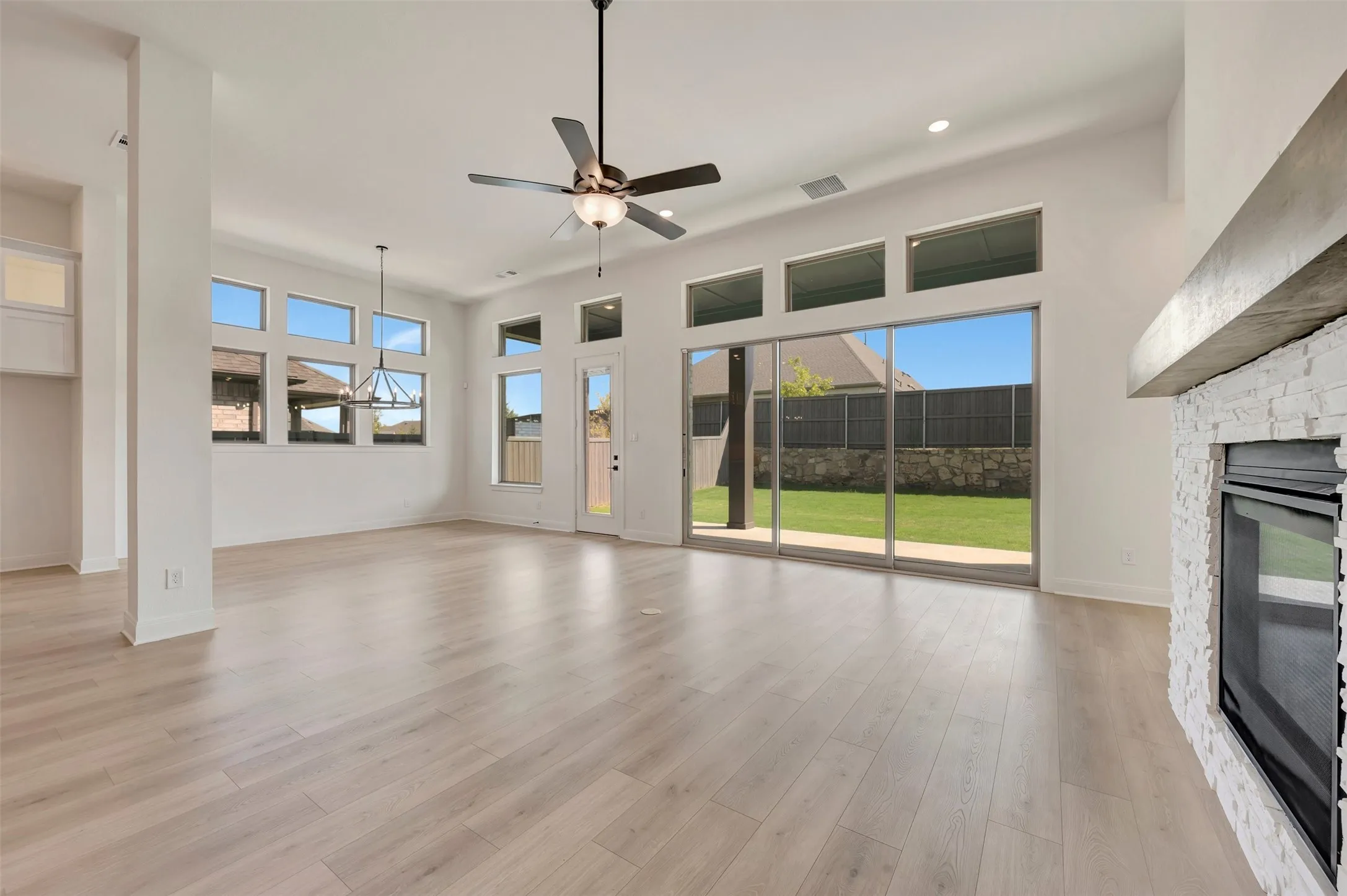Spacious room featuring wood-finish flooring, a contemporary fireplace with stacked stone surround and concrete mantel, and a multi-pane glass sliding door opening to a private backyard
