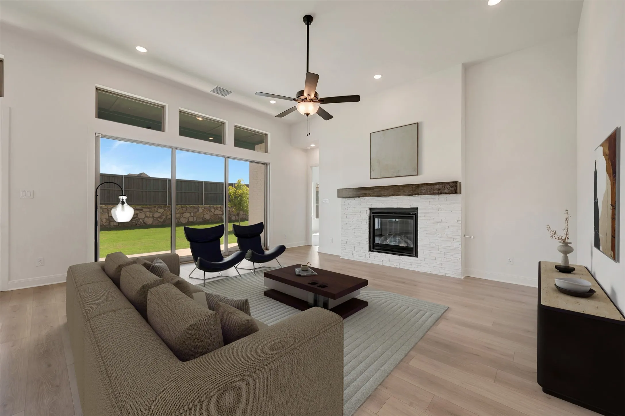 Spacious living area featuring high ceilings, wood-finish flooring, and a fireplace with a stone surround and wood mantel