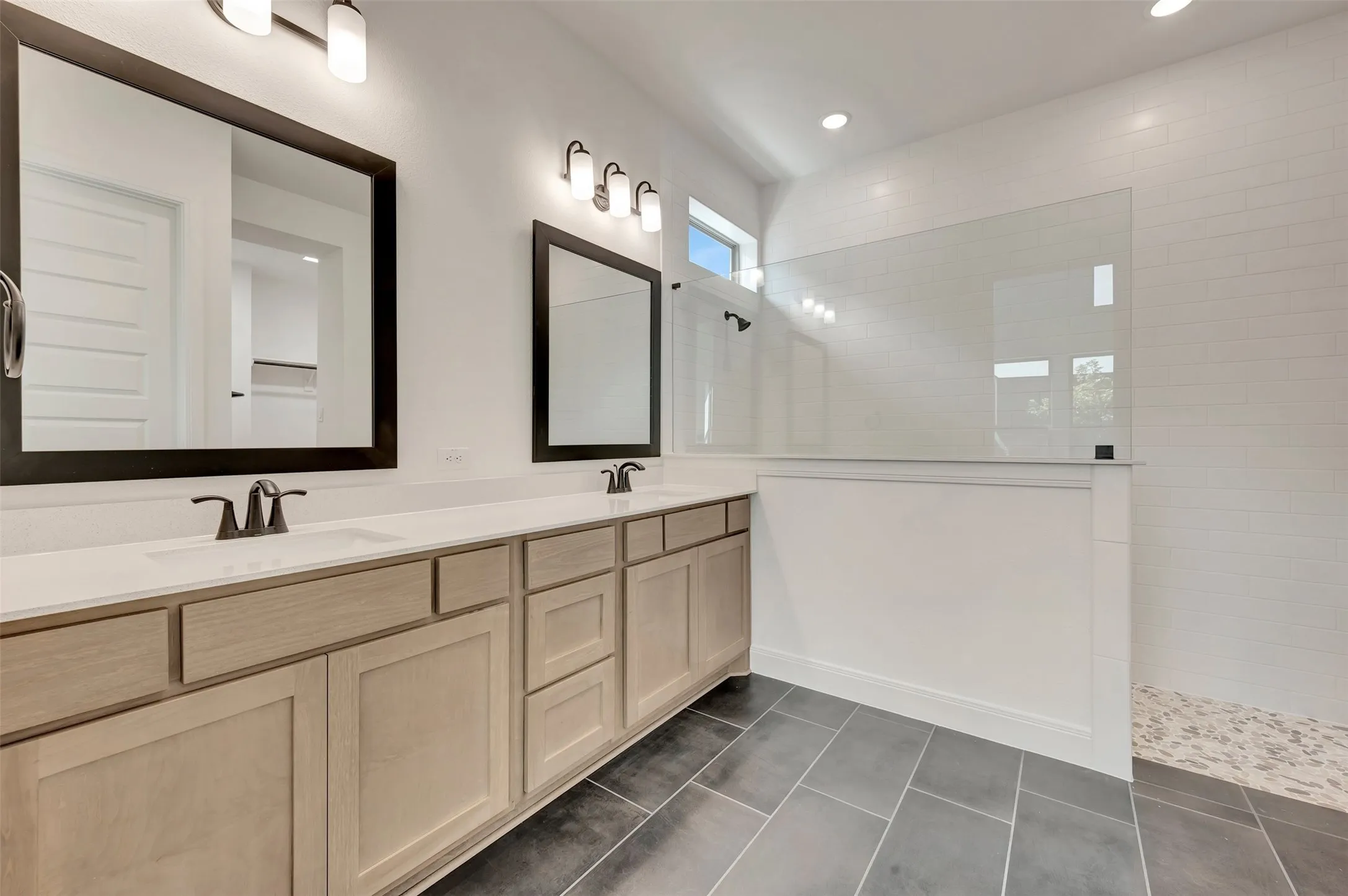 Dual vanity featuring light wood-finish cabinetry, white countertops, and framed mirrors