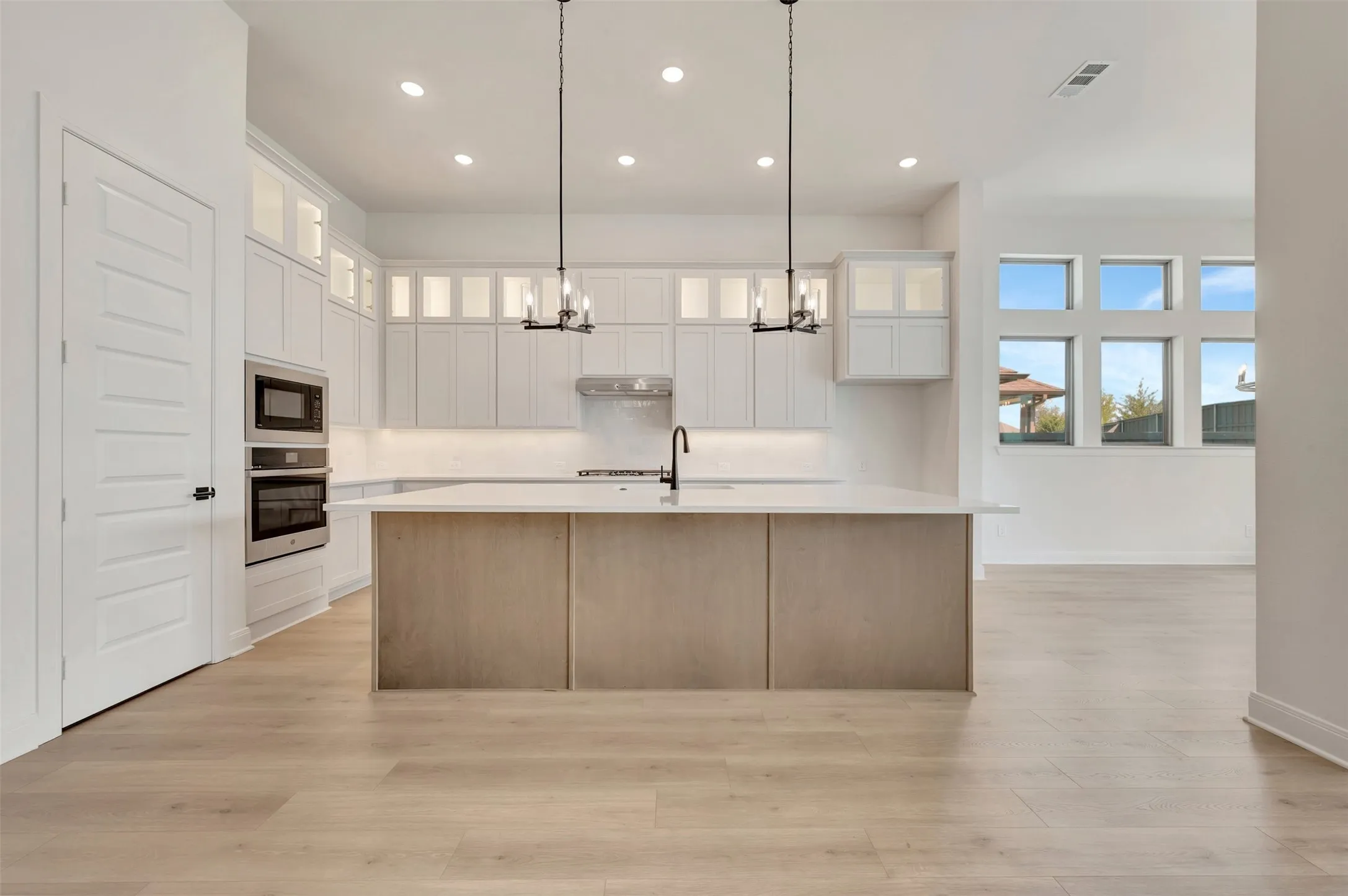 Modern kitchen featuring white cabinetry with glass-front uppers, stainless steel appliances, and a central island with a light wood-finish base and white countertop