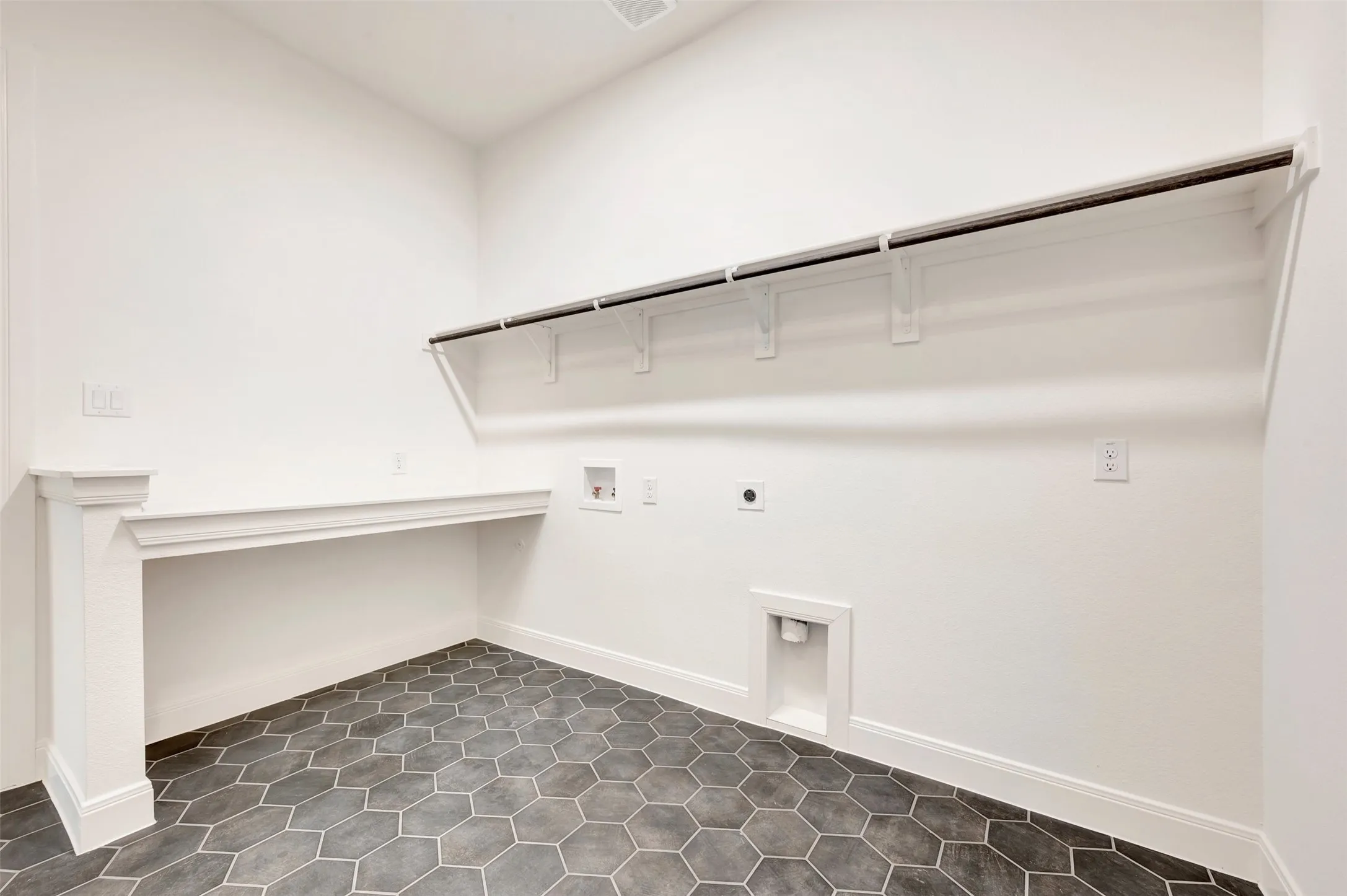 Utility room featuring dark hexagonal tile flooring, a built-in white countertop, white baseboards, and a clothing rod with shelving