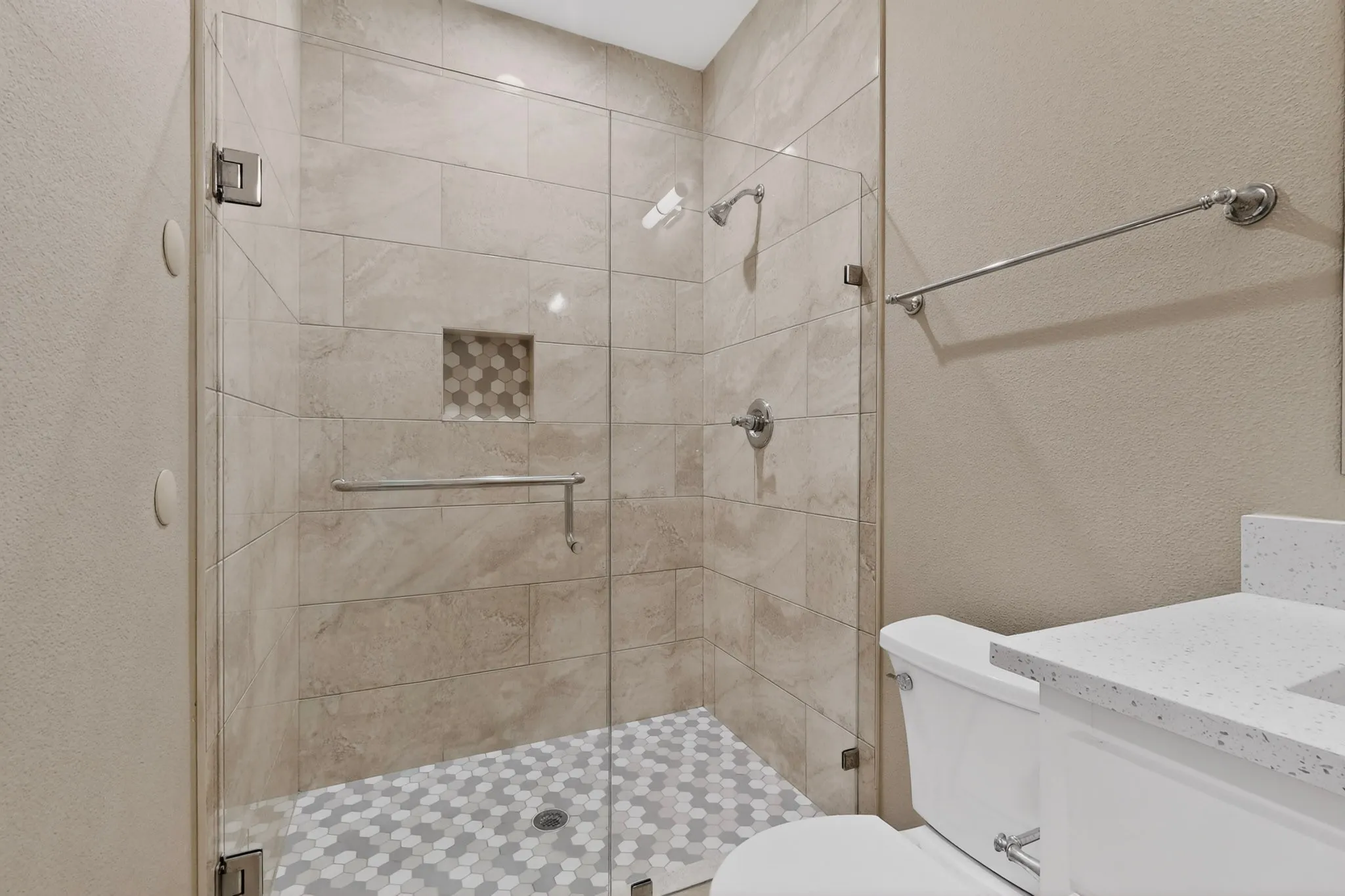 Glass-enclosed shower featuring large format wall tiles and a hexagonal mosaic floor