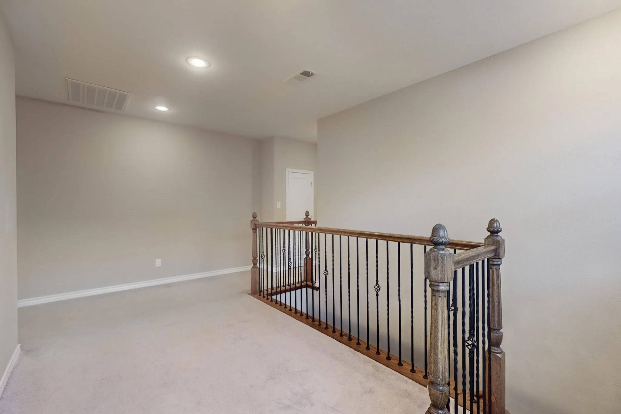 Carpeted landing with recessed lighting, light-toned walls, and a wood railing with wrought iron balusters