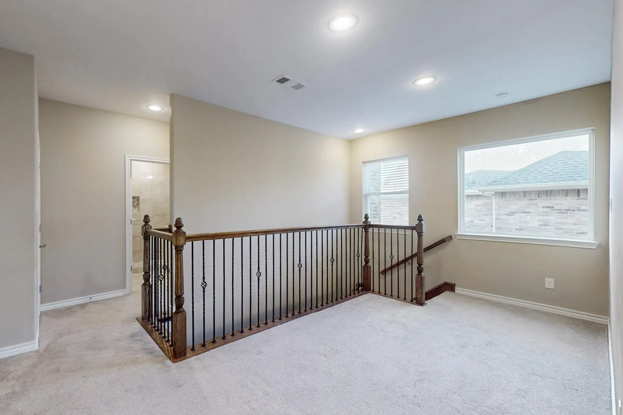 Carpeted landing featuring a wood-and-wrought-iron staircase railing, recessed lighting, and two windows with blinds