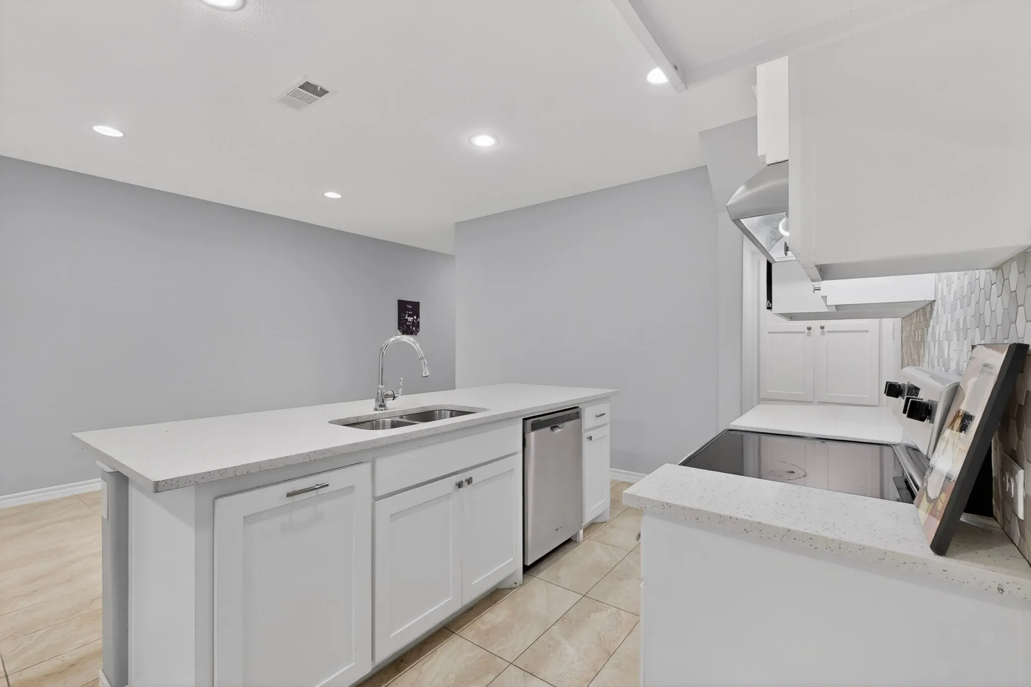 Kitchen featuring white cabinetry, light-toned countertops, a stainless steel dishwasher, a built-in electric cooktop, and an overhead range hood