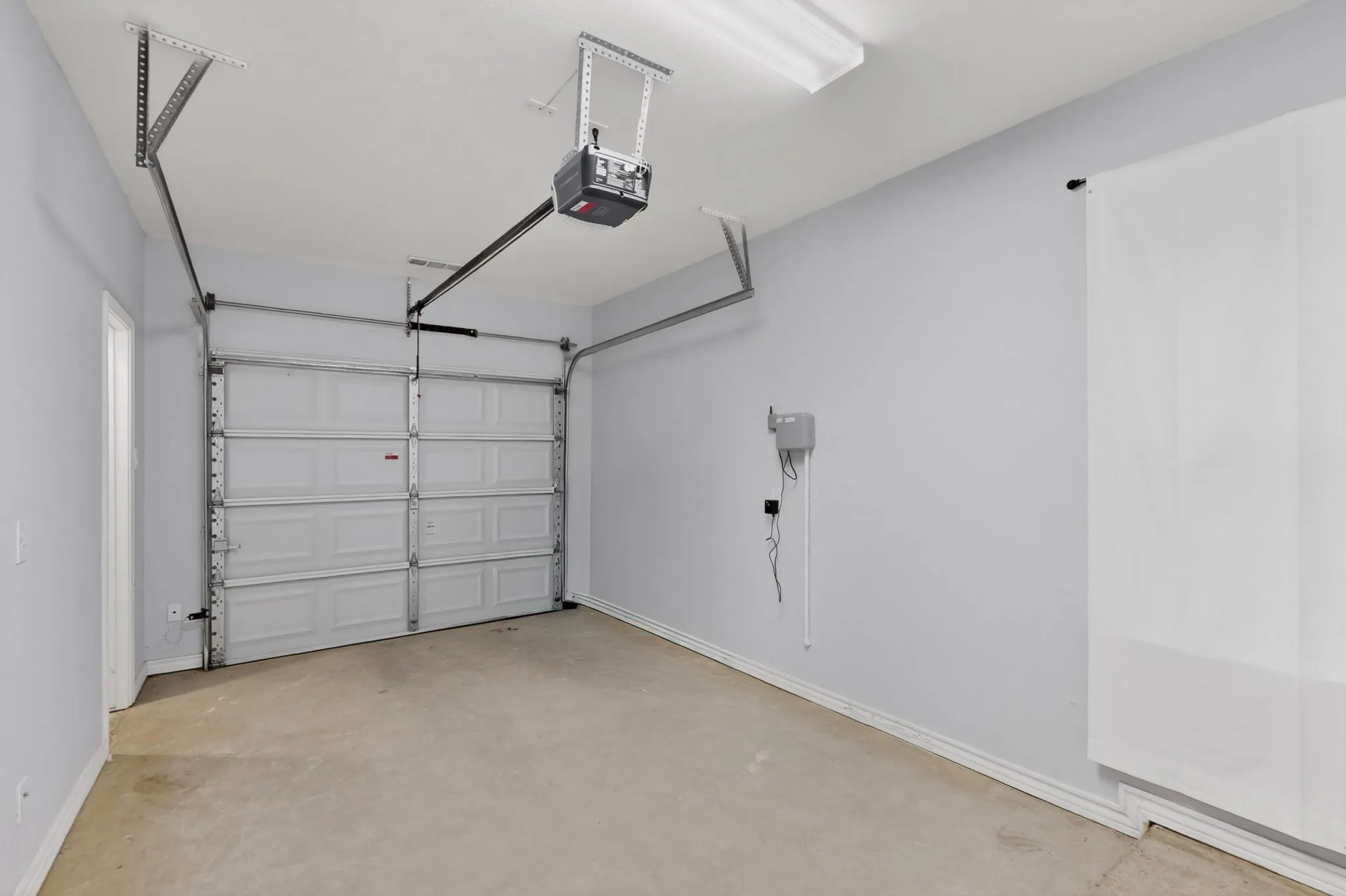 Single-car garage featuring a paneled door with an automatic opener, concrete flooring, and overhead fluorescent lighting