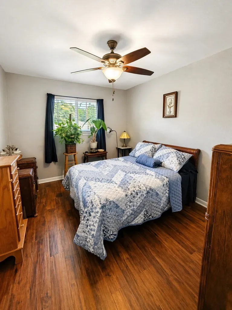 Bedroom featuring wood-finish flooring, a ceiling fan with integrated lighting, and a single window with blinds