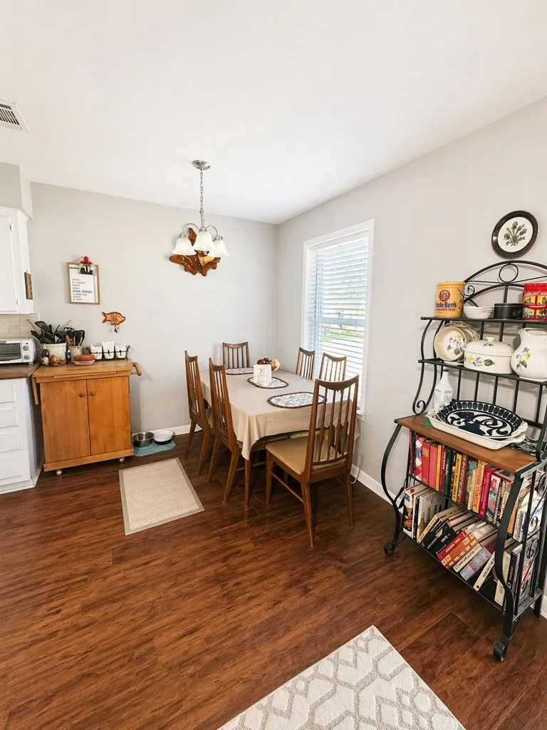 Dining area featuring wood-finish flooring, a chandelier, and ample natural light from a window with blinds