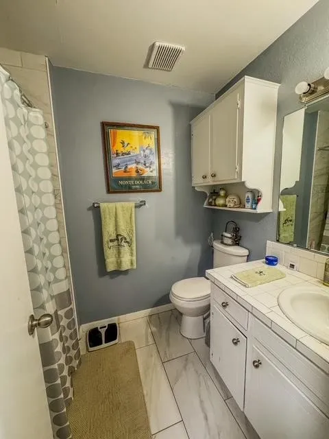 Bathroom featuring white tile-look flooring, a toilet, and a vanity with a drop-in sink