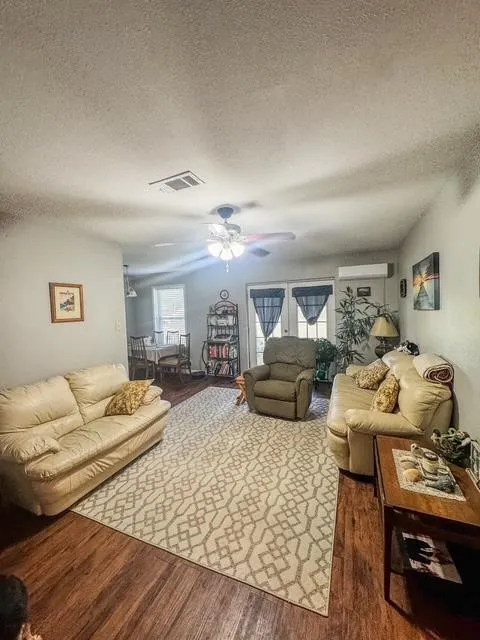 Spacious living area featuring rich wood-finish flooring, a ceiling fan, and light-toned walls