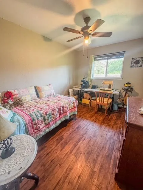 Room featuring wood-finish flooring, a ceiling fan with integrated lighting, and a window providing natural illumination