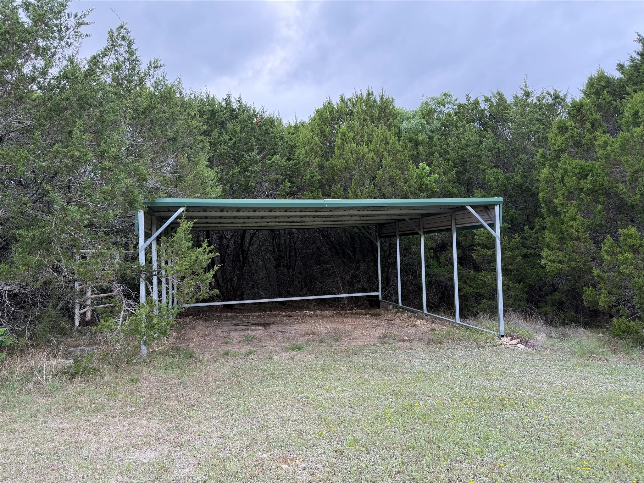 Carport structure with a green metal roof, set on a natural ground surface. Could be used as a stall equipment storage or carport.