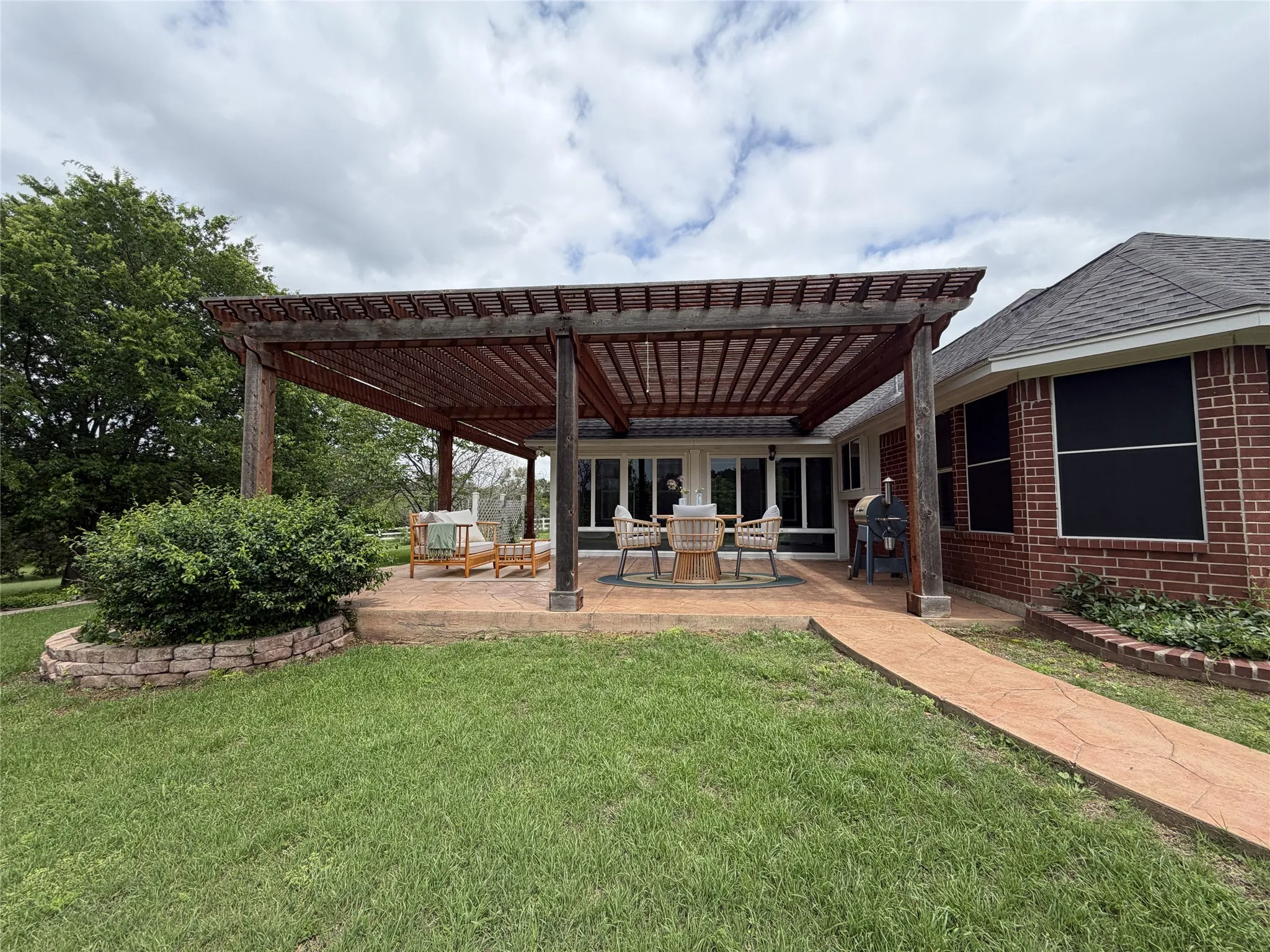 Expansive backyard patio featuring a large wooden pergola, a textured concrete patio, and direct access to the interior through a wall of windows