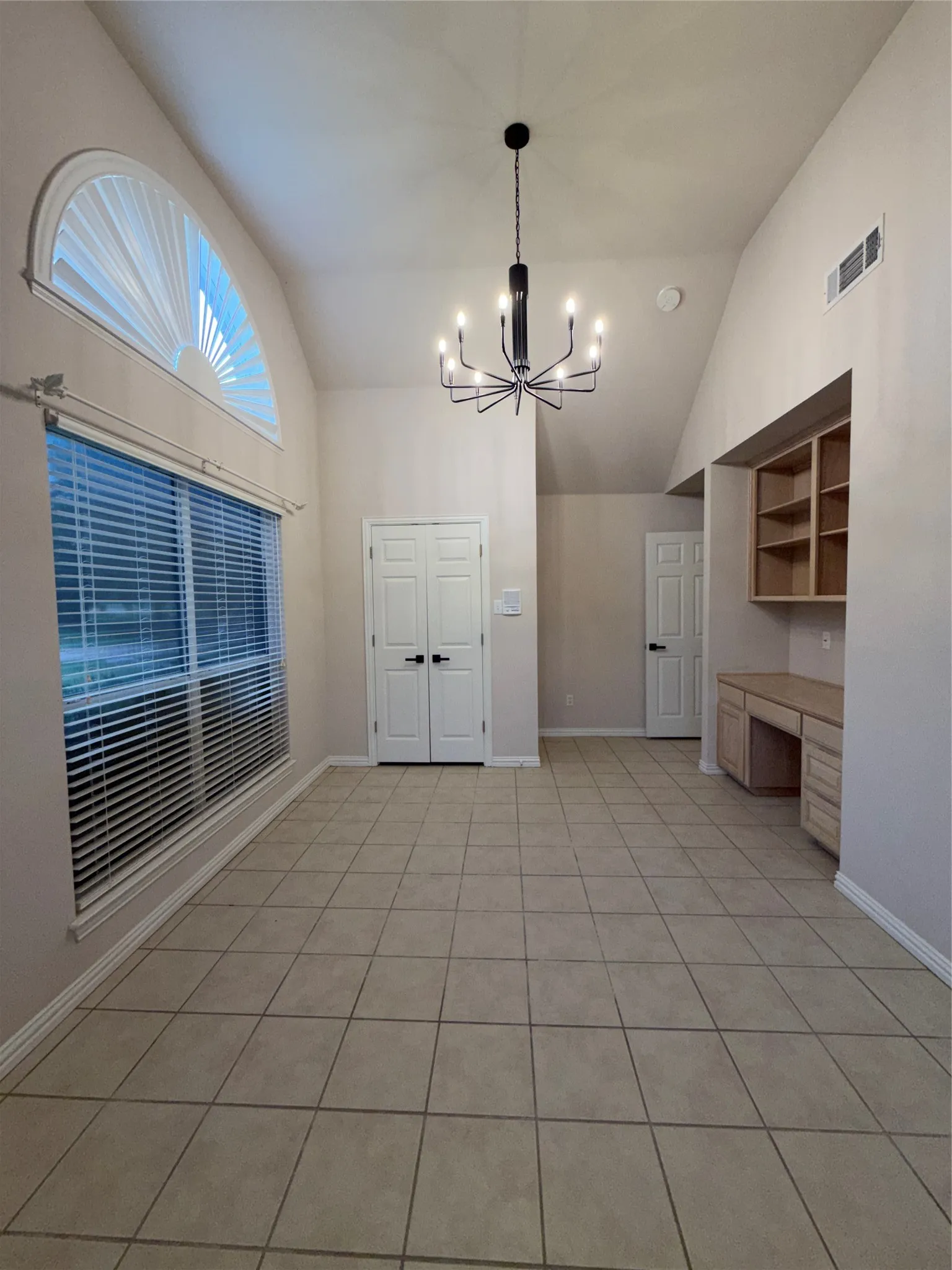 Spacious interior featuring tile flooring, a large window with an arched transom, a contemporary chandelier, built-in desk with shelving, and high vaulted​​‌​​​​‌​​‌‌​‌‌​​​‌‌​‌​‌​‌​​​‌​​ ceilings