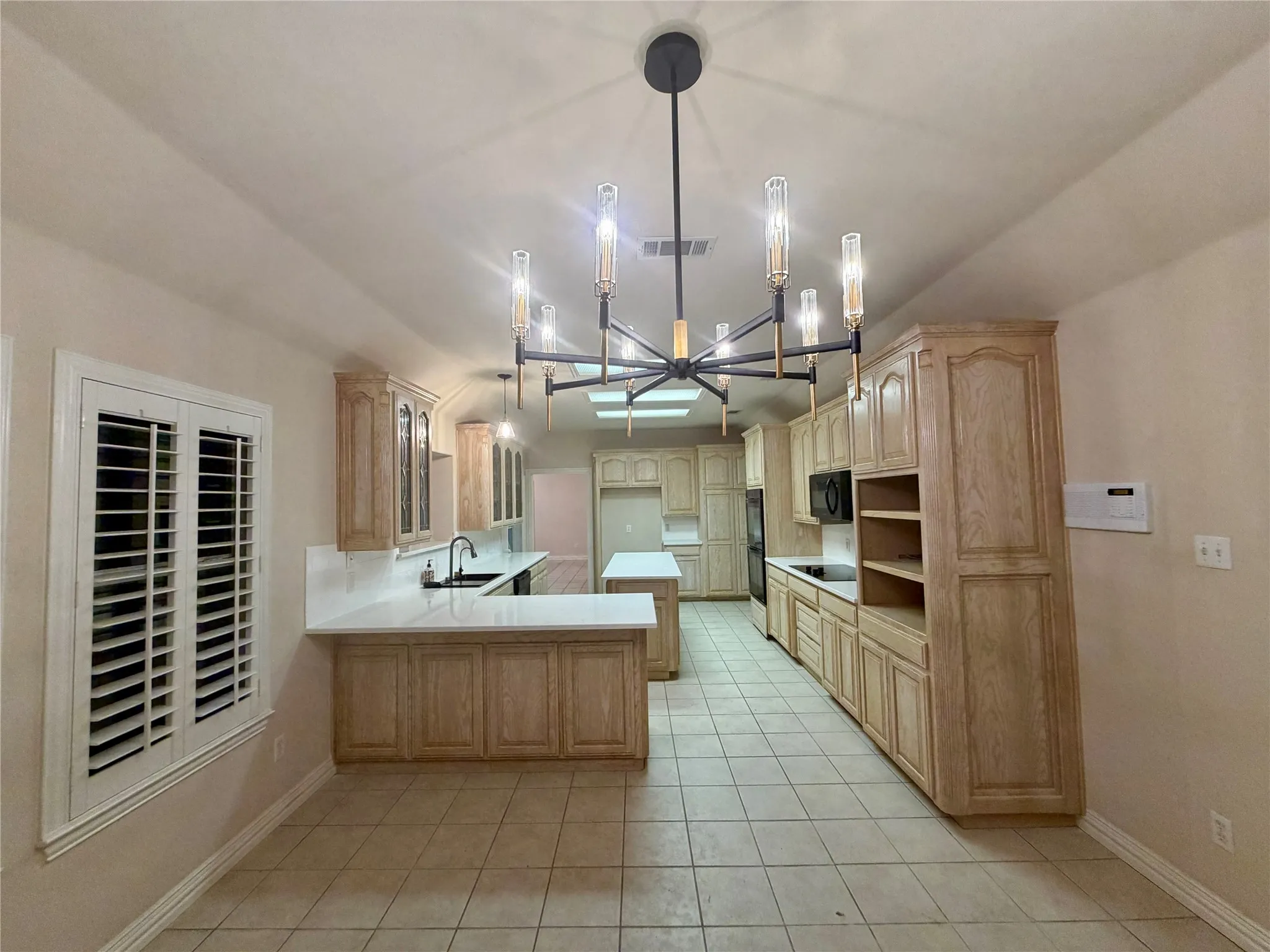 Spacious kitchen featuring extensive wood cabinetry, light-toned countertops, tile flooring, and a contemporary linear chandelier