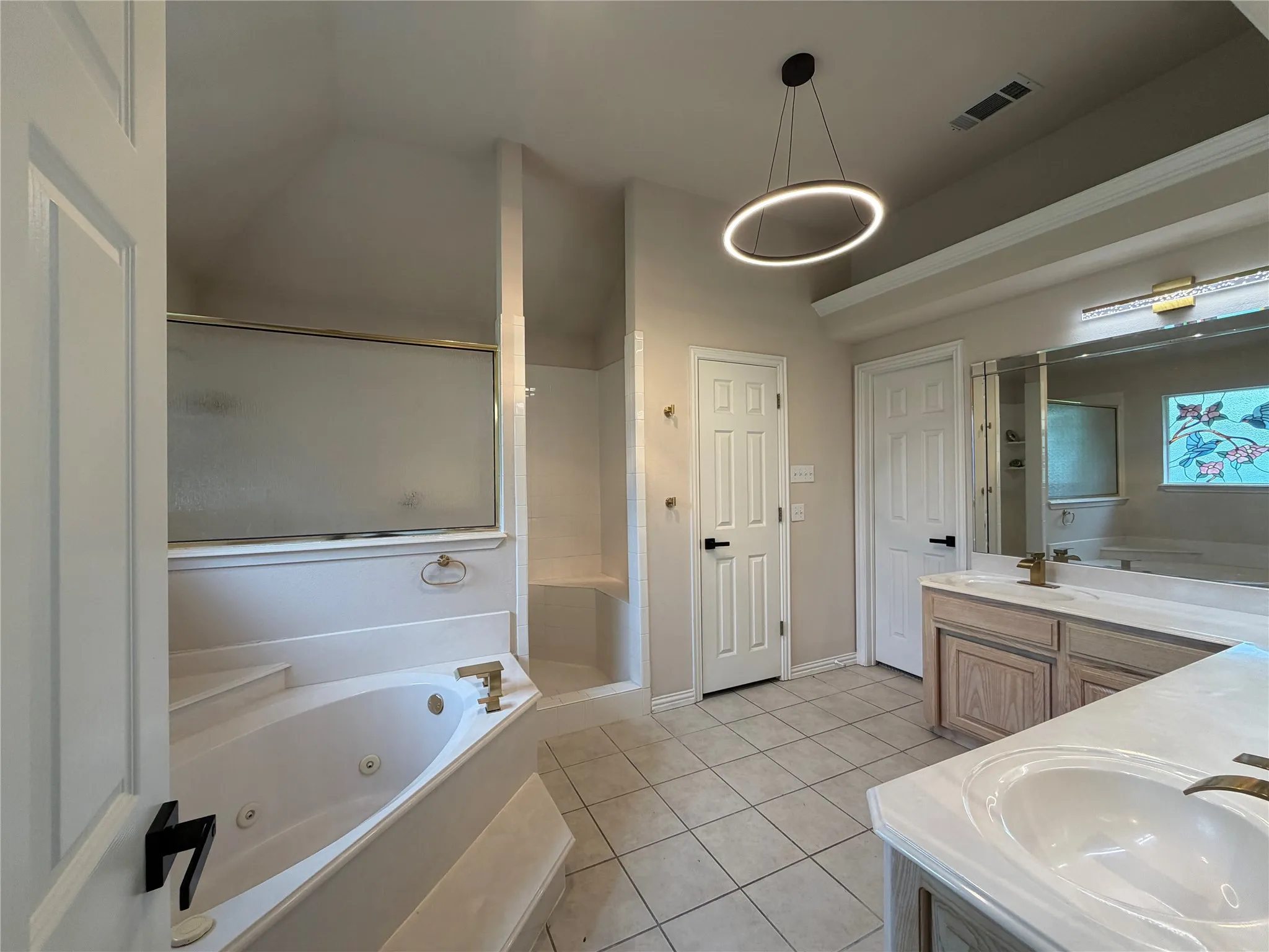 Spacious bathroom featuring a built-in jetted tub, separate shower with frosted glass enclosure, dual vanity, toilet room and closet off of bathroom area