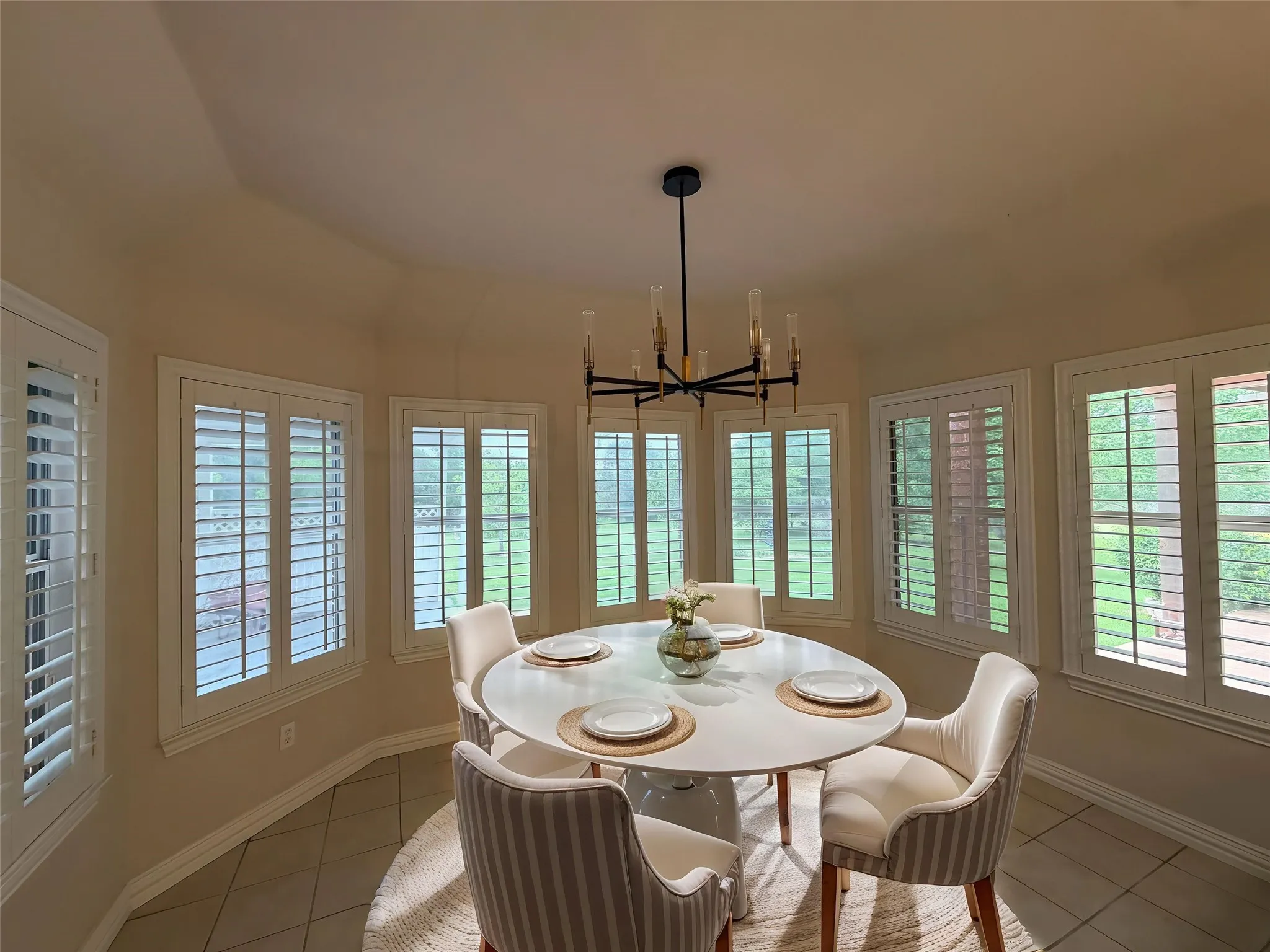 Wrap around window in dining area / breakfast nook featuring extensive plantation shutters, a contemporary black and gold chandelier, and tile flooring