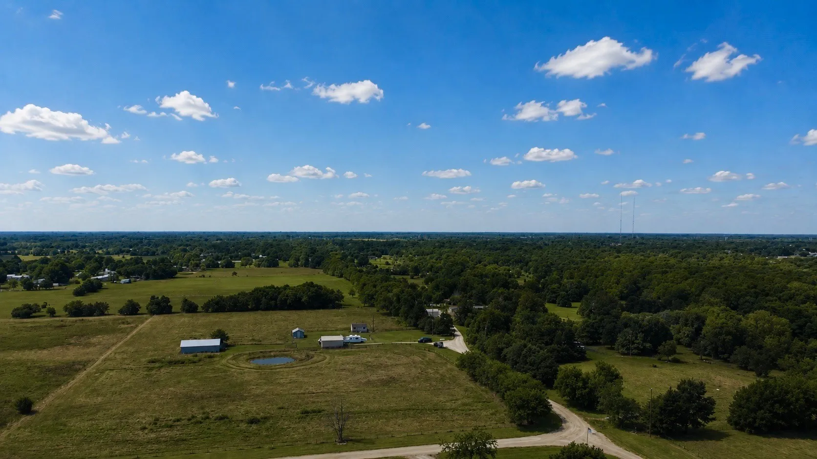 Expansive property featuring a pond, multiple outbuildings, mature trees, and open fields