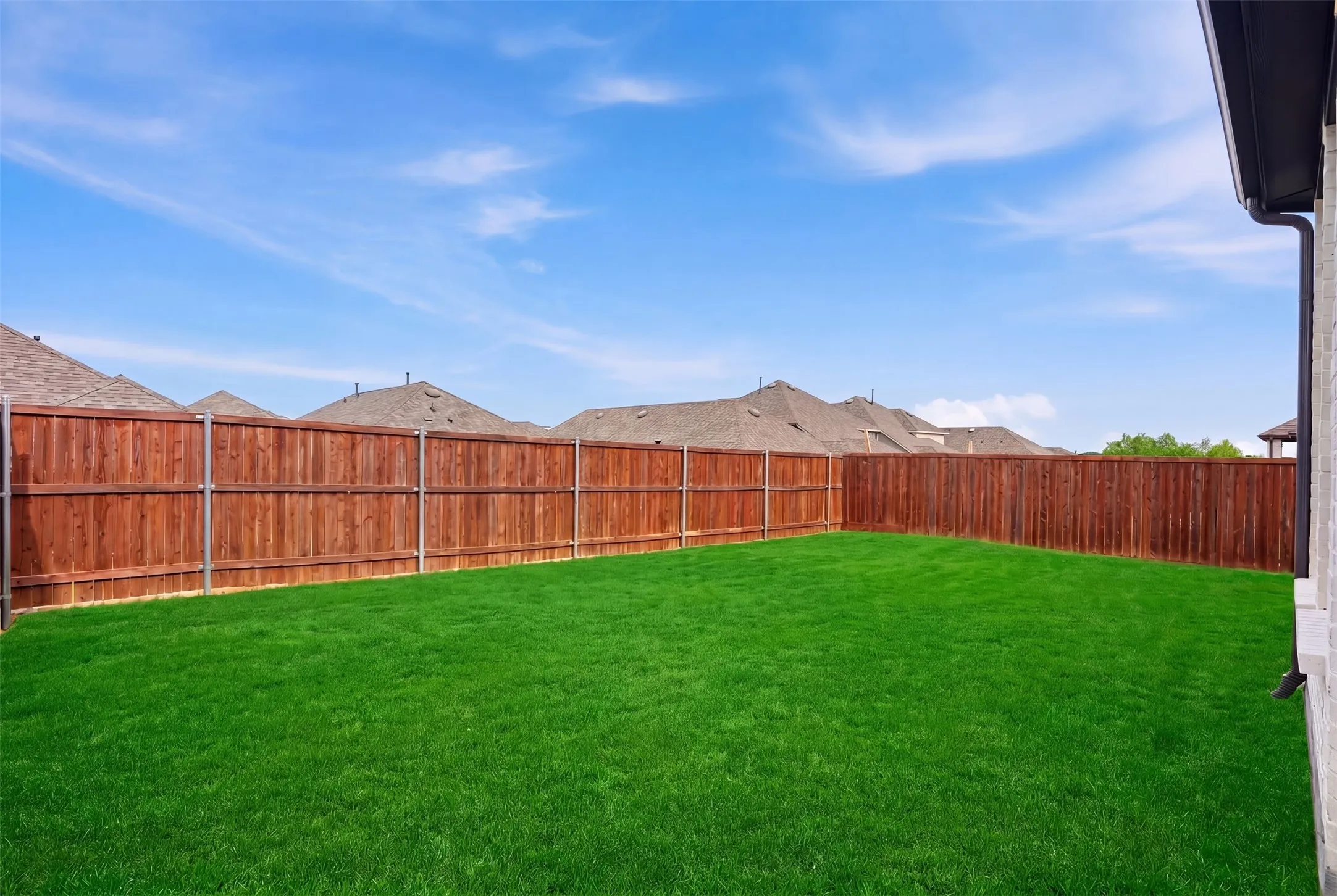 Spacious backyard featuring a lush green lawn, fully fenced perimeter with wood privacy fencing, and a side exterior wall of the property