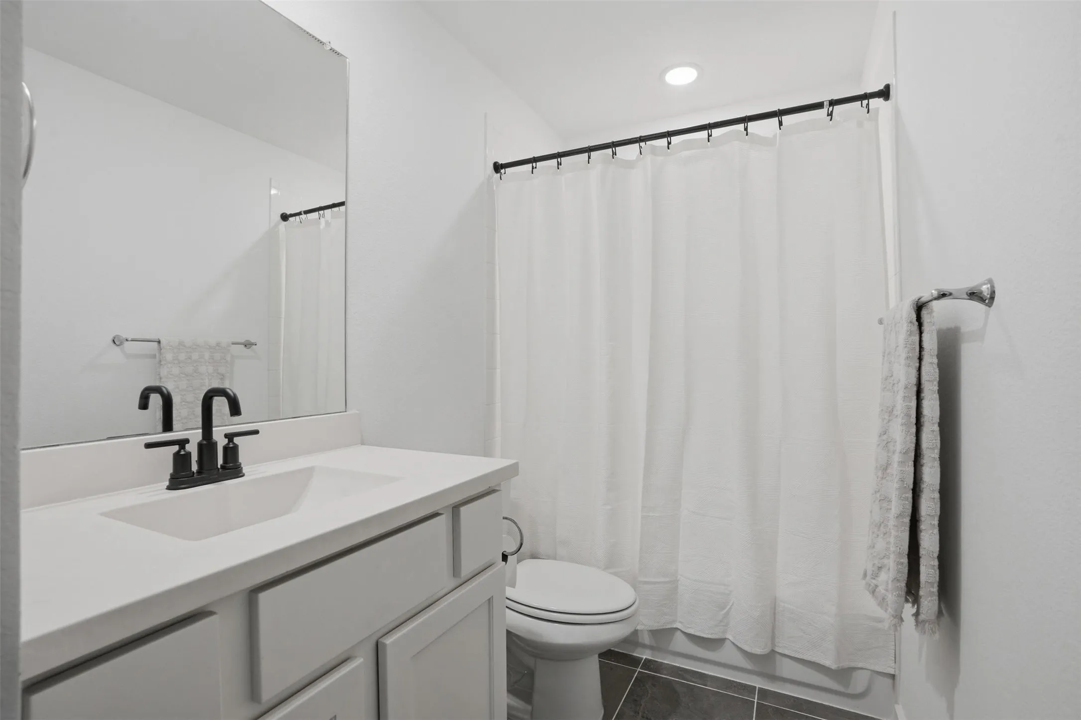 White vanity with integrated sink, matte black faucet, and frameless mirror