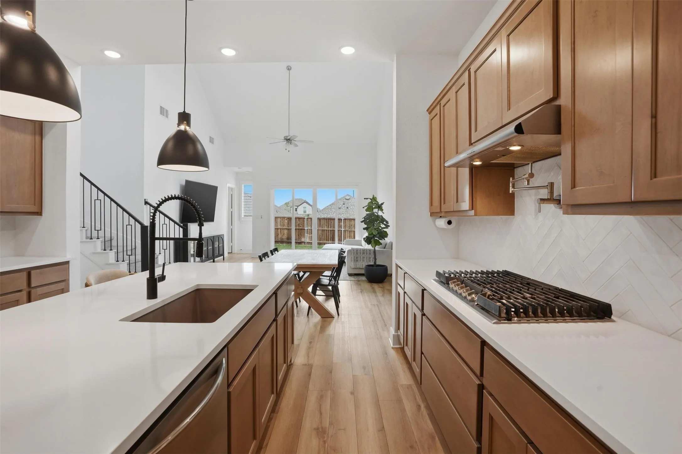 Expansive kitchen island with a copper-tone sink and matte black faucet, complemented by light wood-finish cabinetry, white countertops, and a herringbone-patterned backsplash