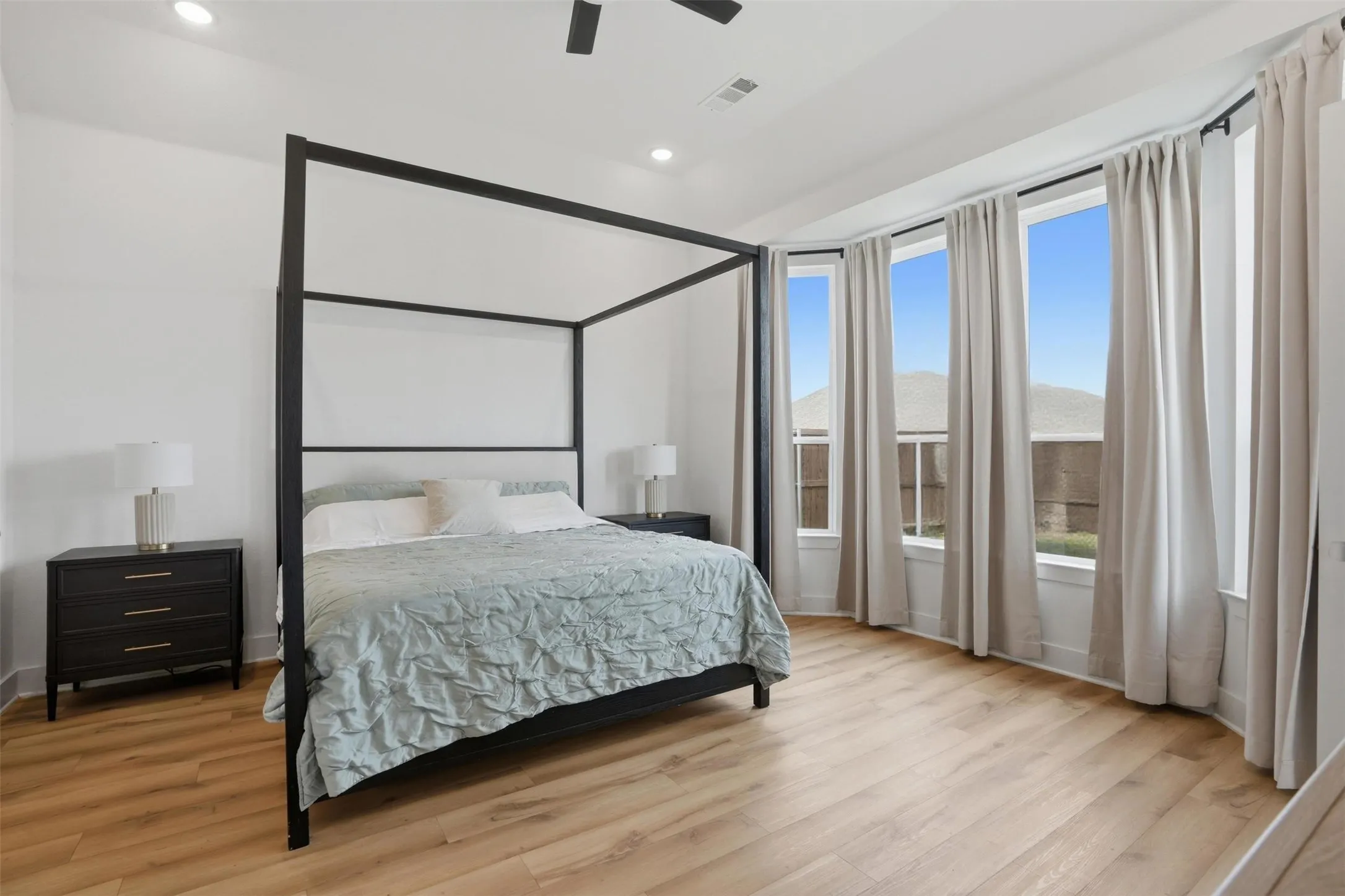 Spacious room featuring light wood-finish flooring, a bay window with multiple vertical windows, recessed lighting, and a ceiling fan