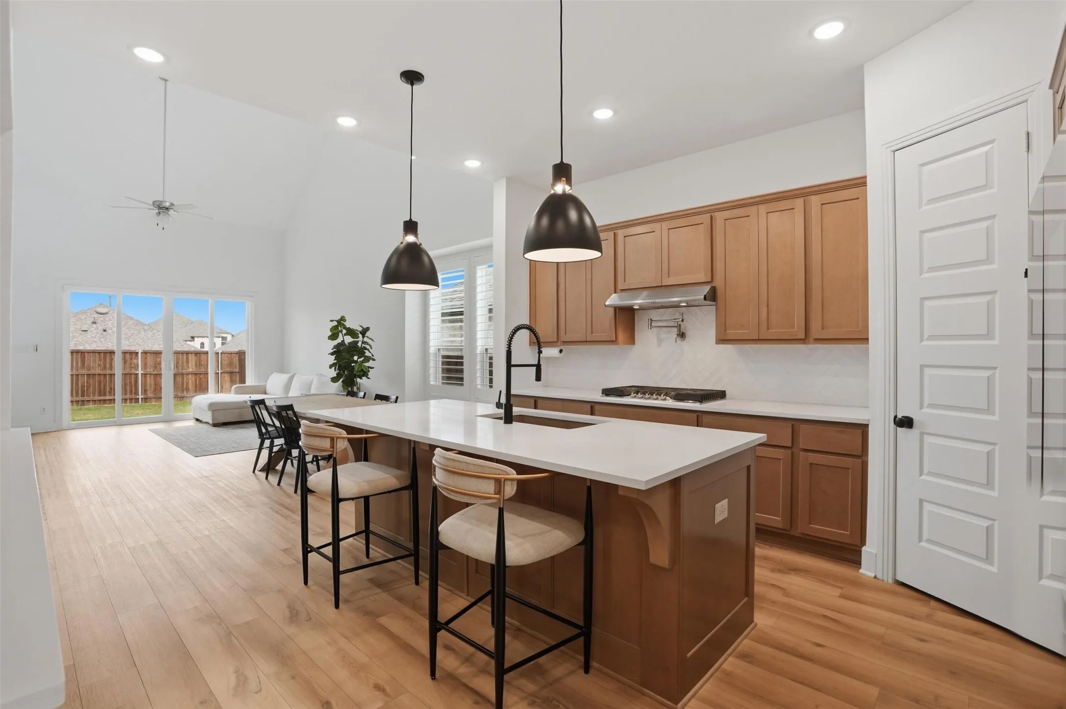 Open-concept living space featuring a kitchen island with pendant lighting, wood-finish flooring, vaulted ceilings, and sliding glass doors leading to the backyard