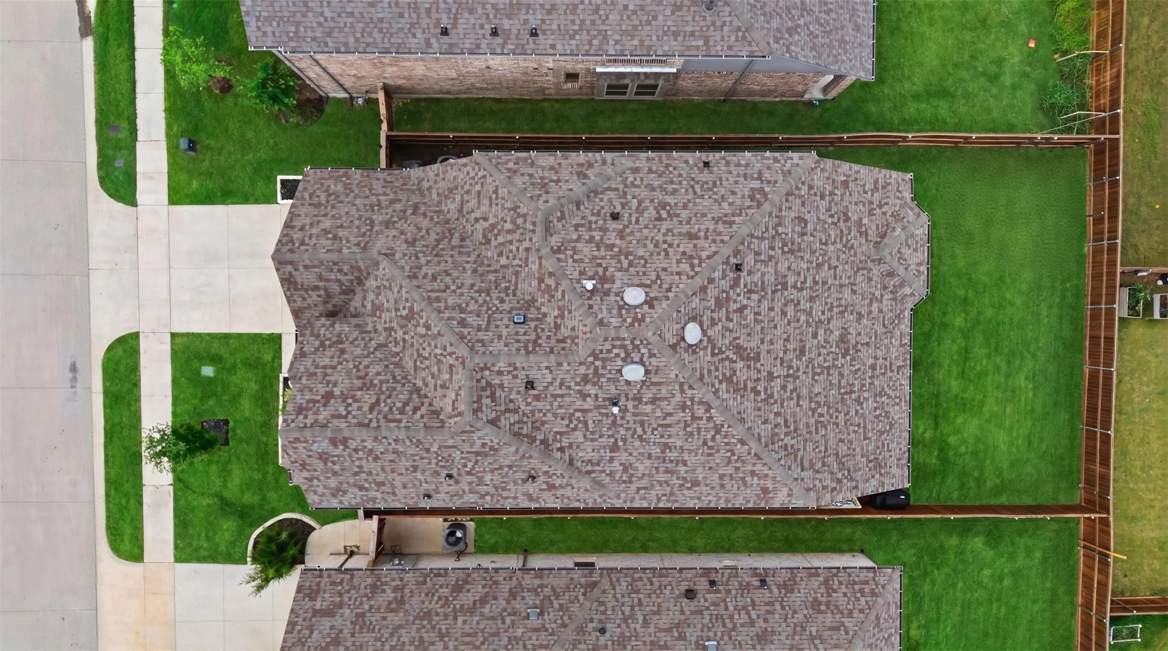 Overhead property view featuring a shingle roof with multiple vents, a concrete driveway and sidewalk, and a fenced backyard with green lawn