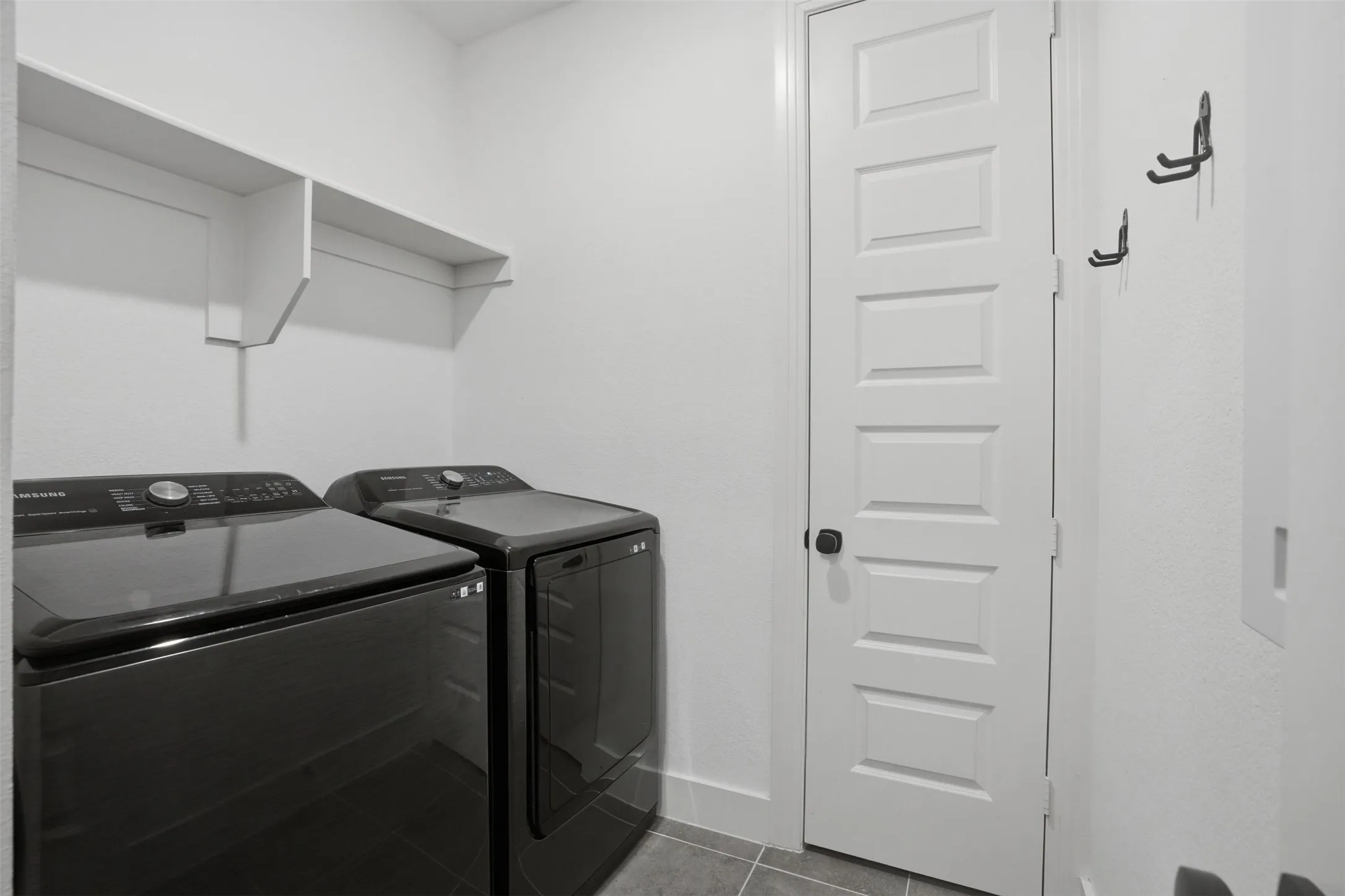 Laundry area featuring a built-in shelving unit, white paneled door with dark hardware, and tile flooring