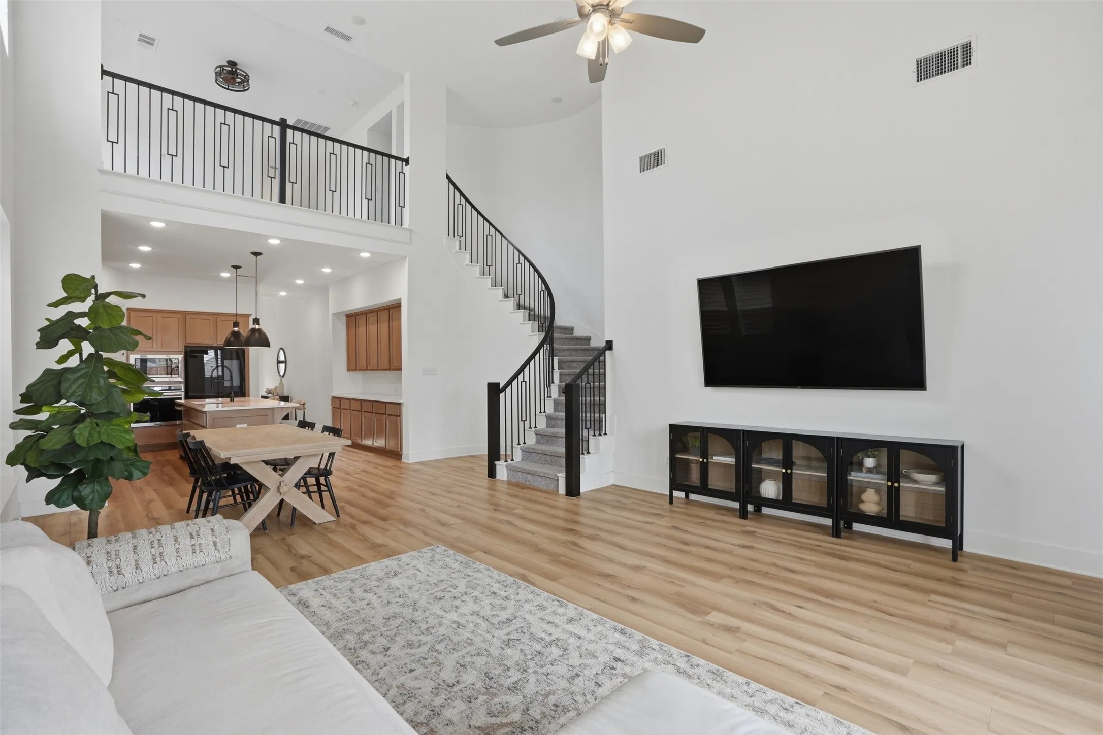 Expansive living area featuring high ceilings, wood-finish flooring, and a curved staircase with wrought iron balusters