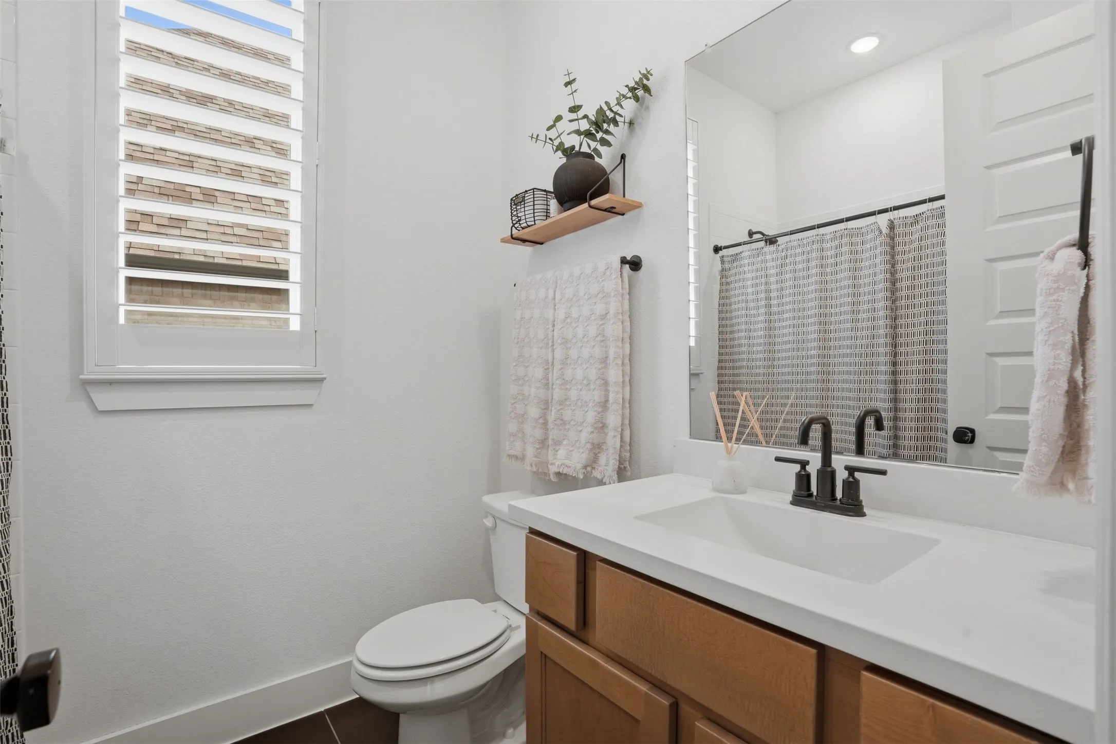 Bathroom featuring a single vanity with wood-finish cabinetry and a white countertop, matte black faucet, and a large mirror