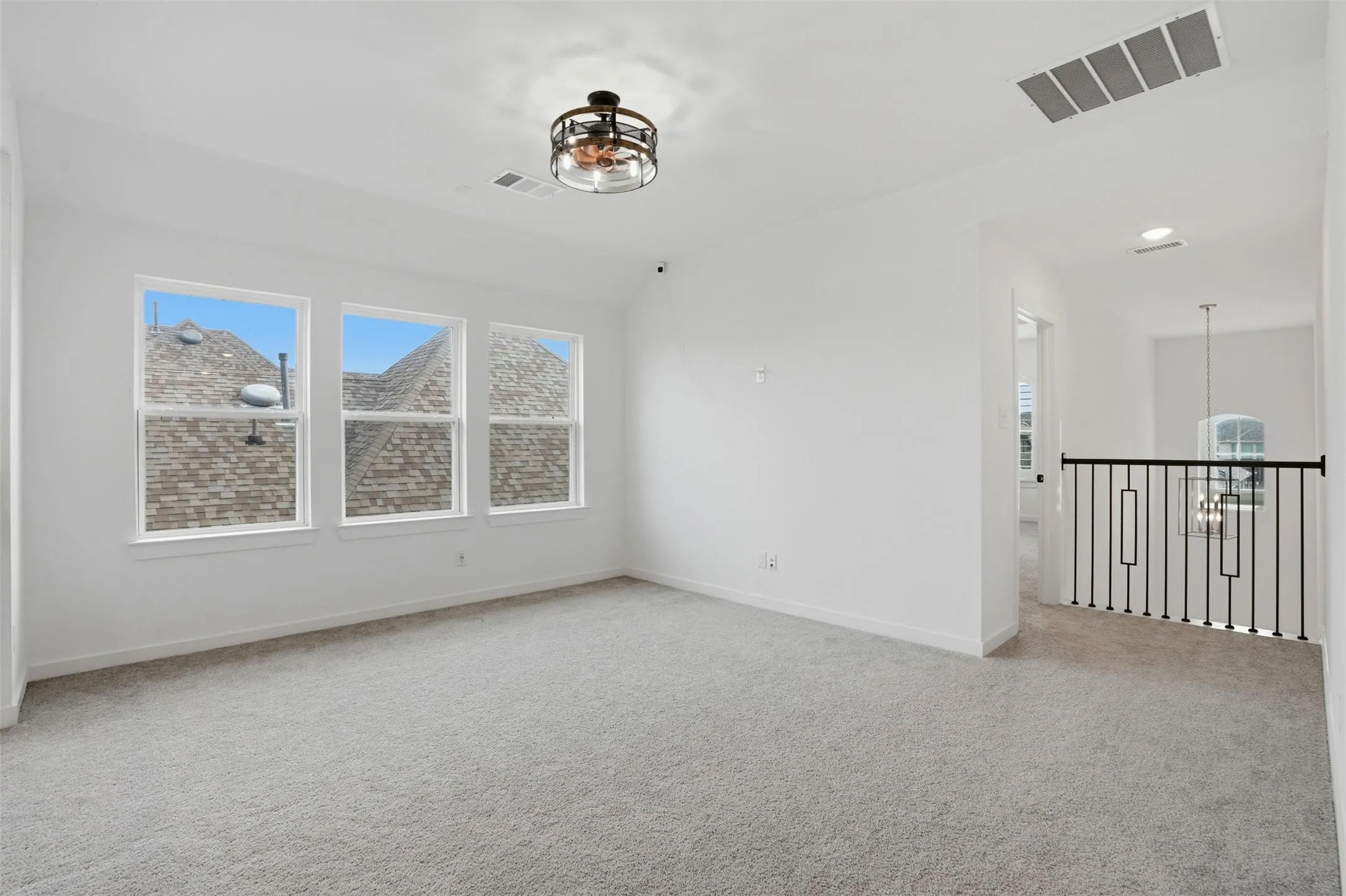 Spacious room featuring three white-framed windows, light gray carpet, and a modern ceiling fan