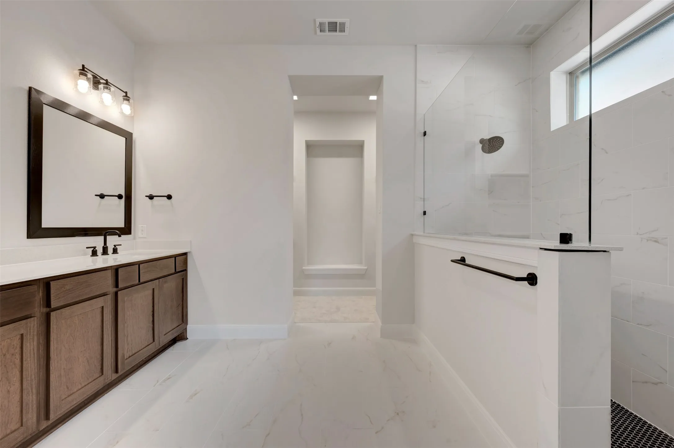 Spacious bathroom featuring a wood-finish vanity with countertop, a large framed mirror, and a glass-enclosed shower with tile surround