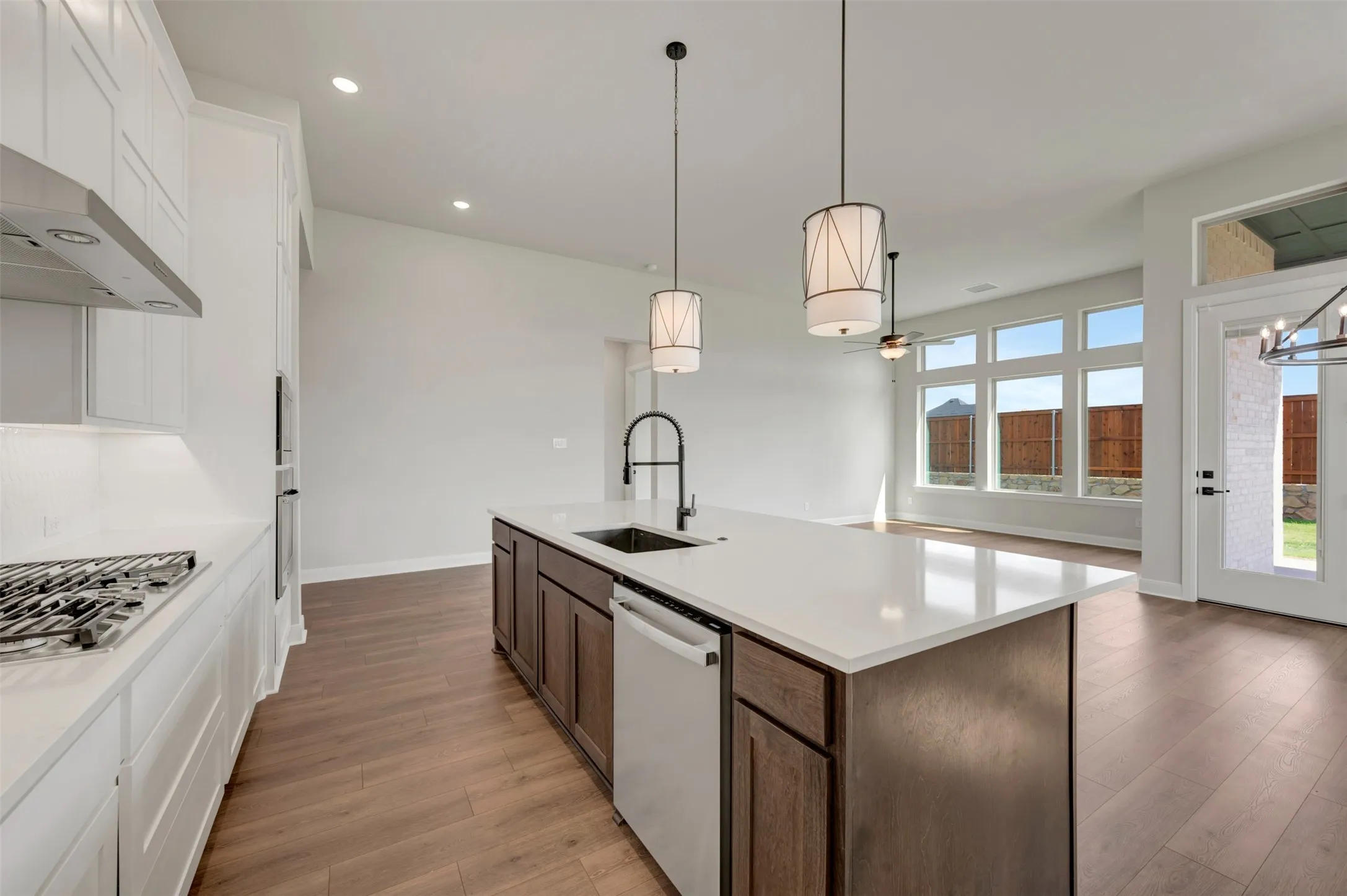 Kitchen island with a built-in sink and pendant lighting, stainless steel appliances, wood-finish flooring, and multiple large windows