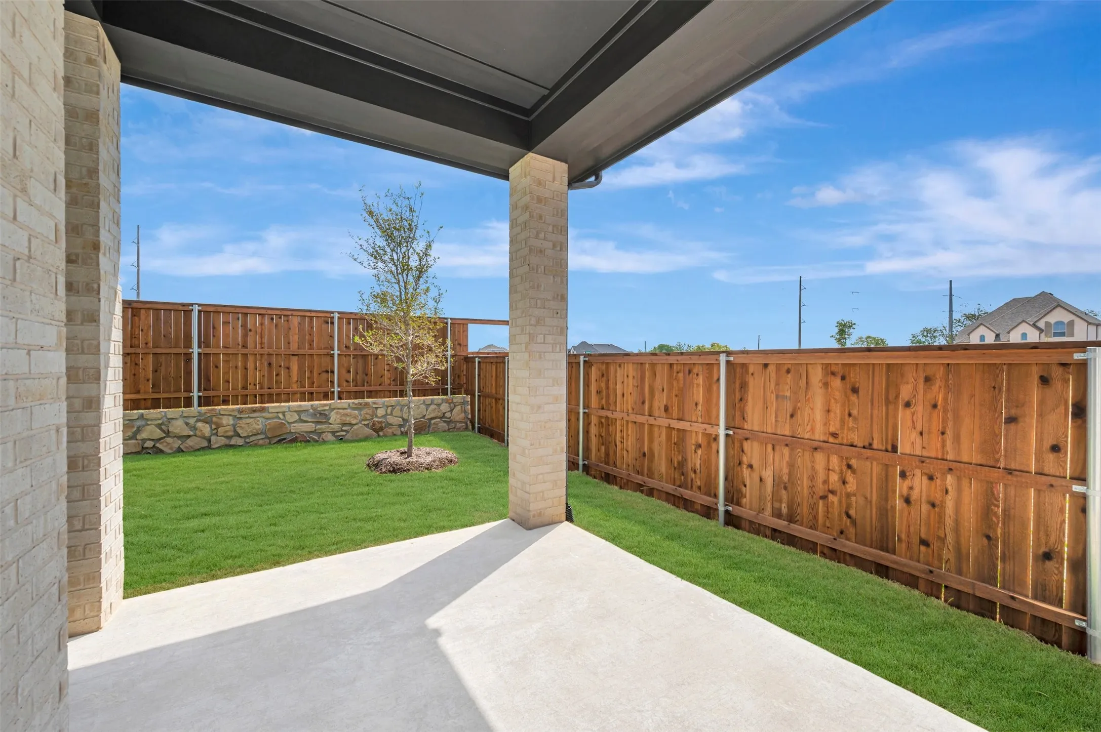 Covered patio with concrete flooring, stone retaining wall, and wood fencing